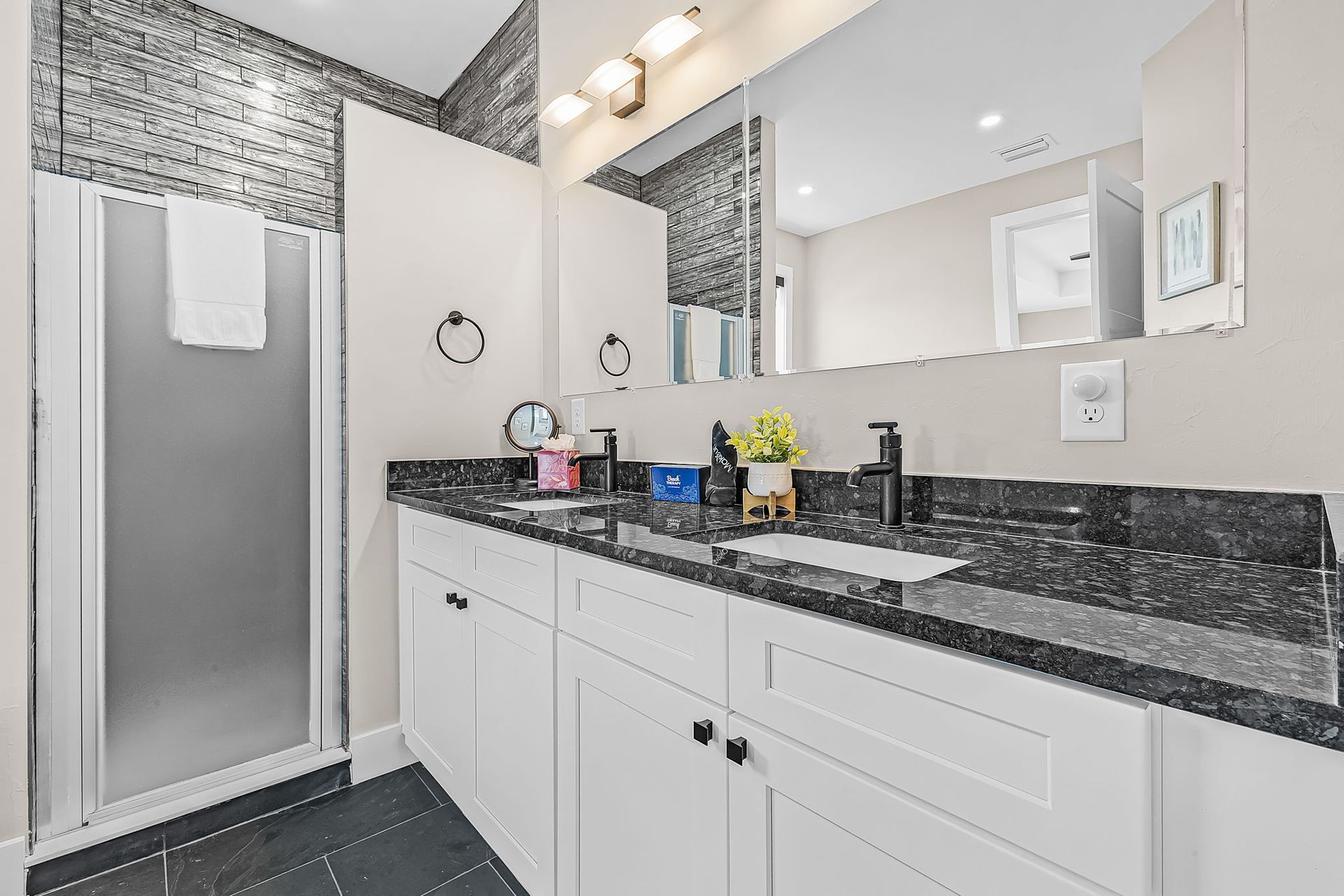 Bright bathroom with white vanity, black granite counter, large mirror, and frosted glass shower.