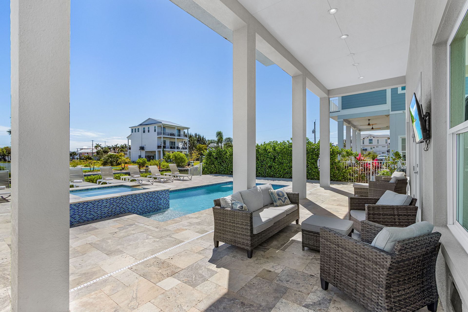Covered patio with wicker chairs overlooking a pool and ocean-view landscaping.
