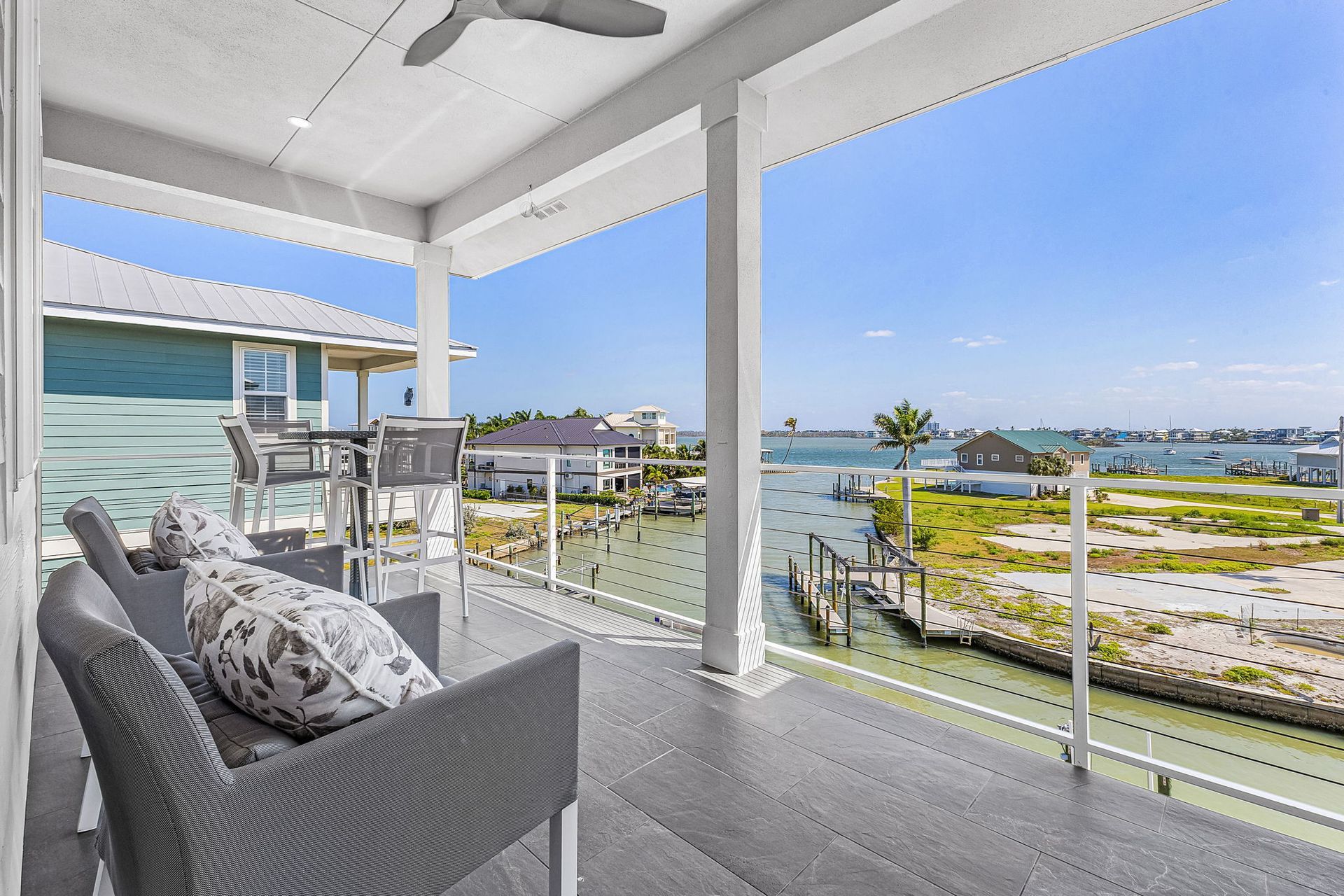 Covered patio with gray seating overlooking a calm waterfront and blue sky.