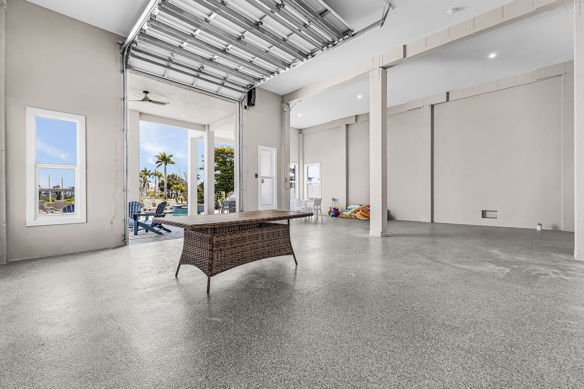 Spacious empty room with polished concrete floor, exposed ceiling beams, and large windows overlooking palm trees.