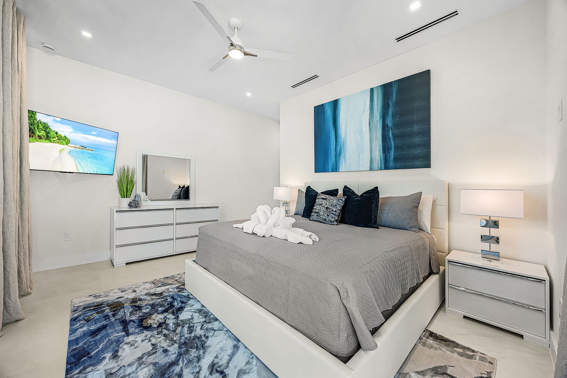 Modern bedroom with gray bed, blue abstract art, and white furniture.