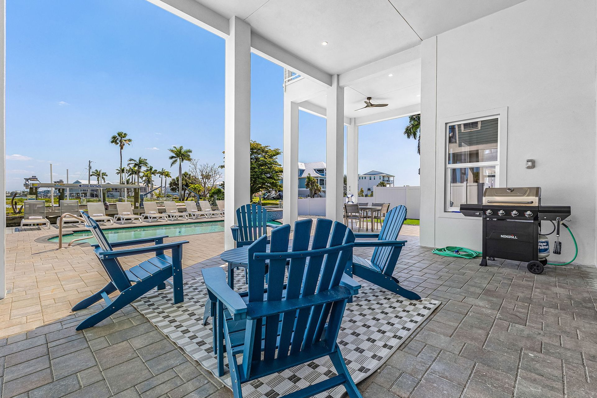 Blue Adirondack chairs on a covered patio overlooking a sunny beachfront courtyard