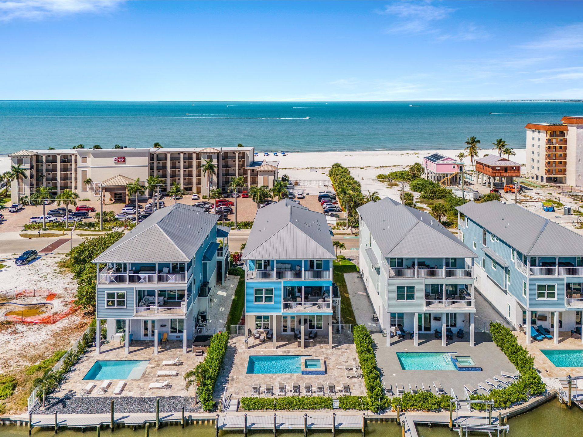 Oceanfront row of blue beach condos with pools, overlooking white sand and turquoise water