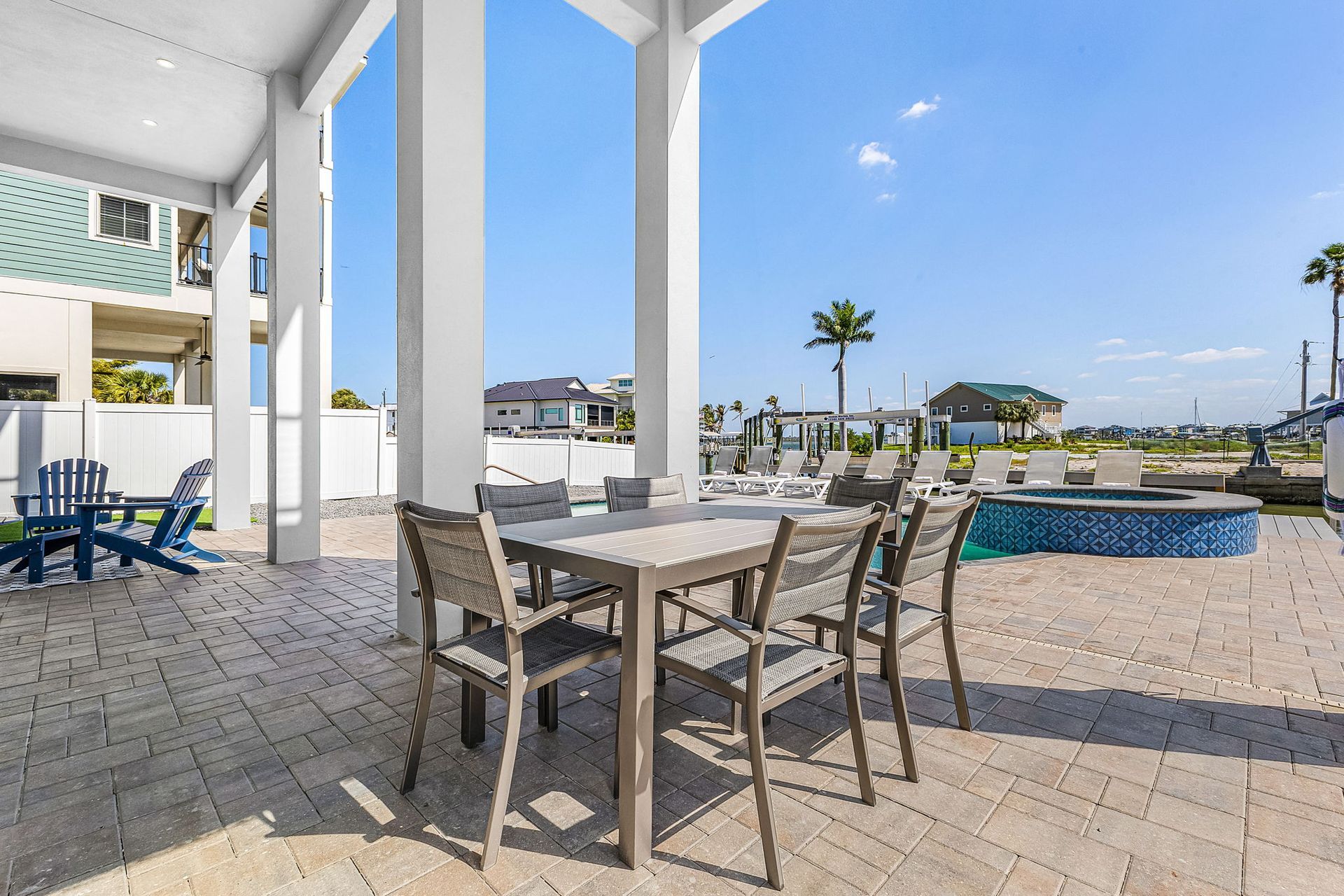 Patio dining area with table and chairs overlooking a sunny waterfront and pool