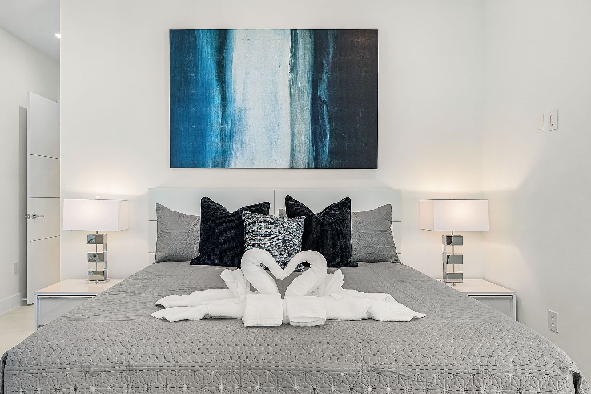 Bedroom with bed, art, bedside tables, lamps, and swan towel art.