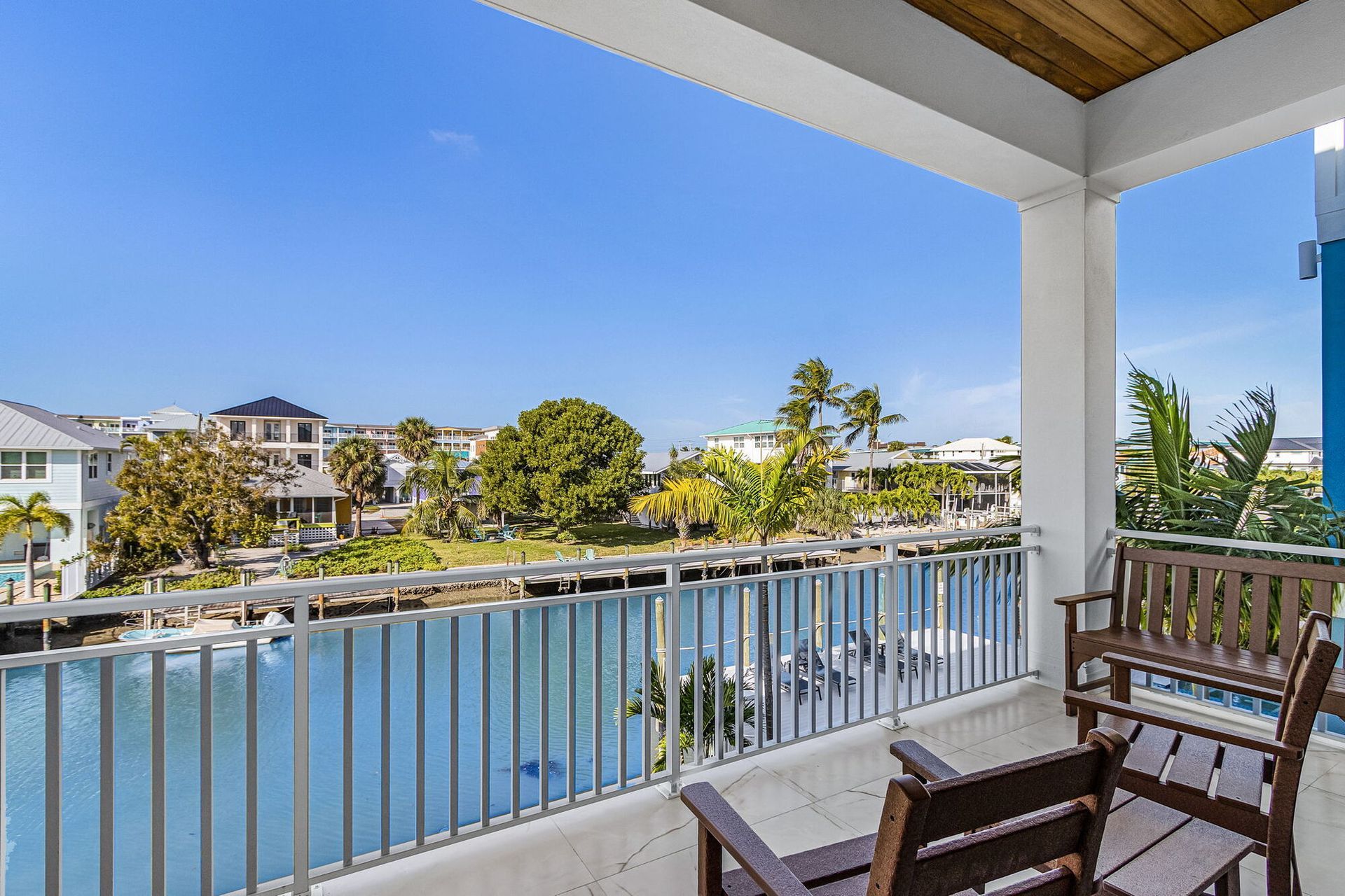 Balcony overlooking a sunny waterfront canal with chairs, railing, and palm trees