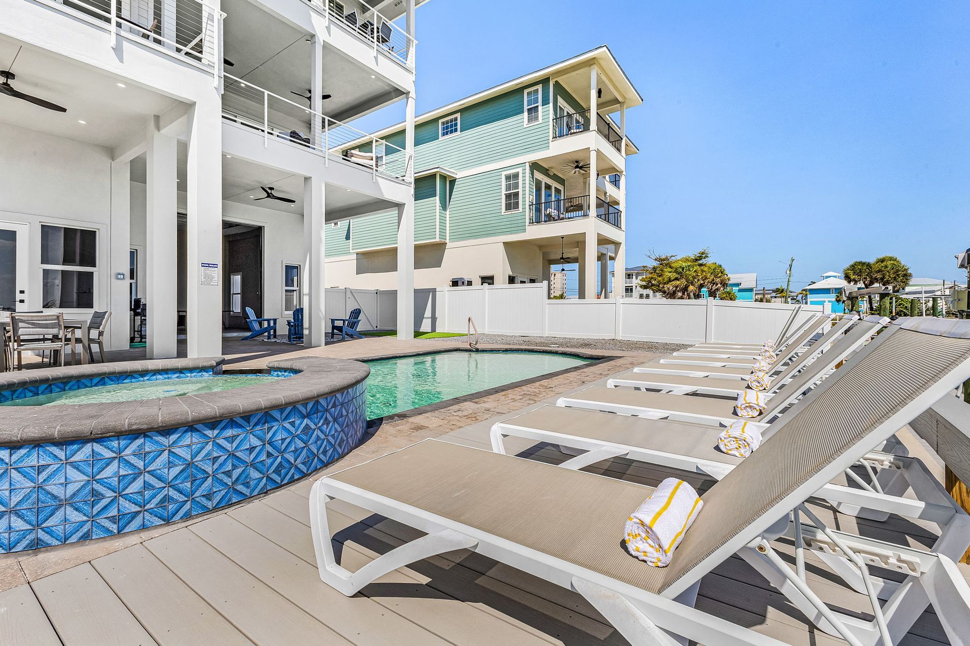Resort pool deck with blue-tiled spa, lounge chairs, and white beachfront buildings under a clear sky
