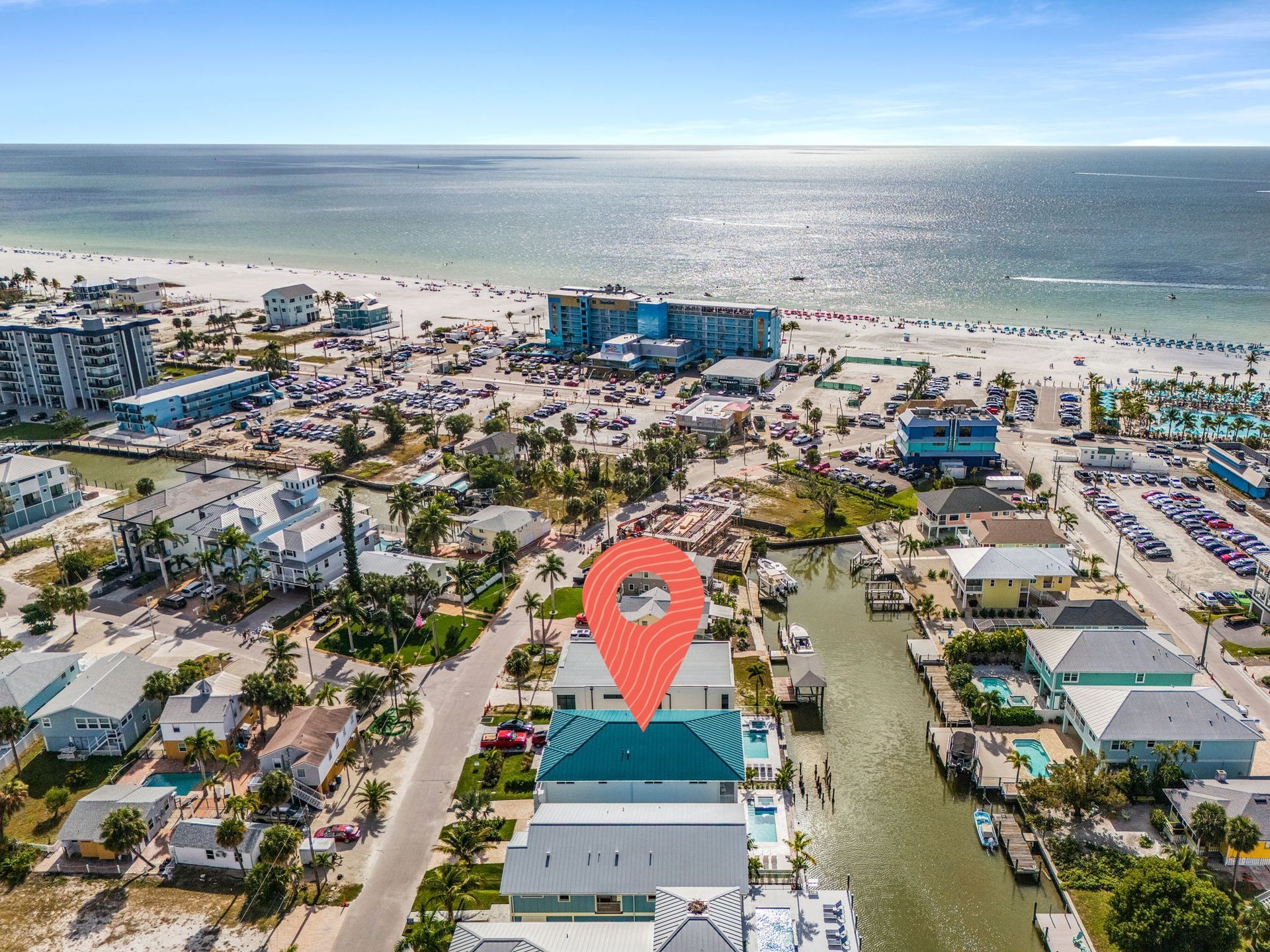 Aerial view of beachside houses, canal, and crowded beach with a location pin.