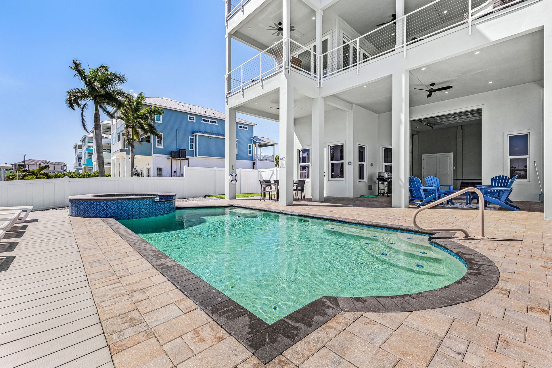 White waterfront patio with a turquoise pool, lounge chairs, and a palm tree beside a modern house