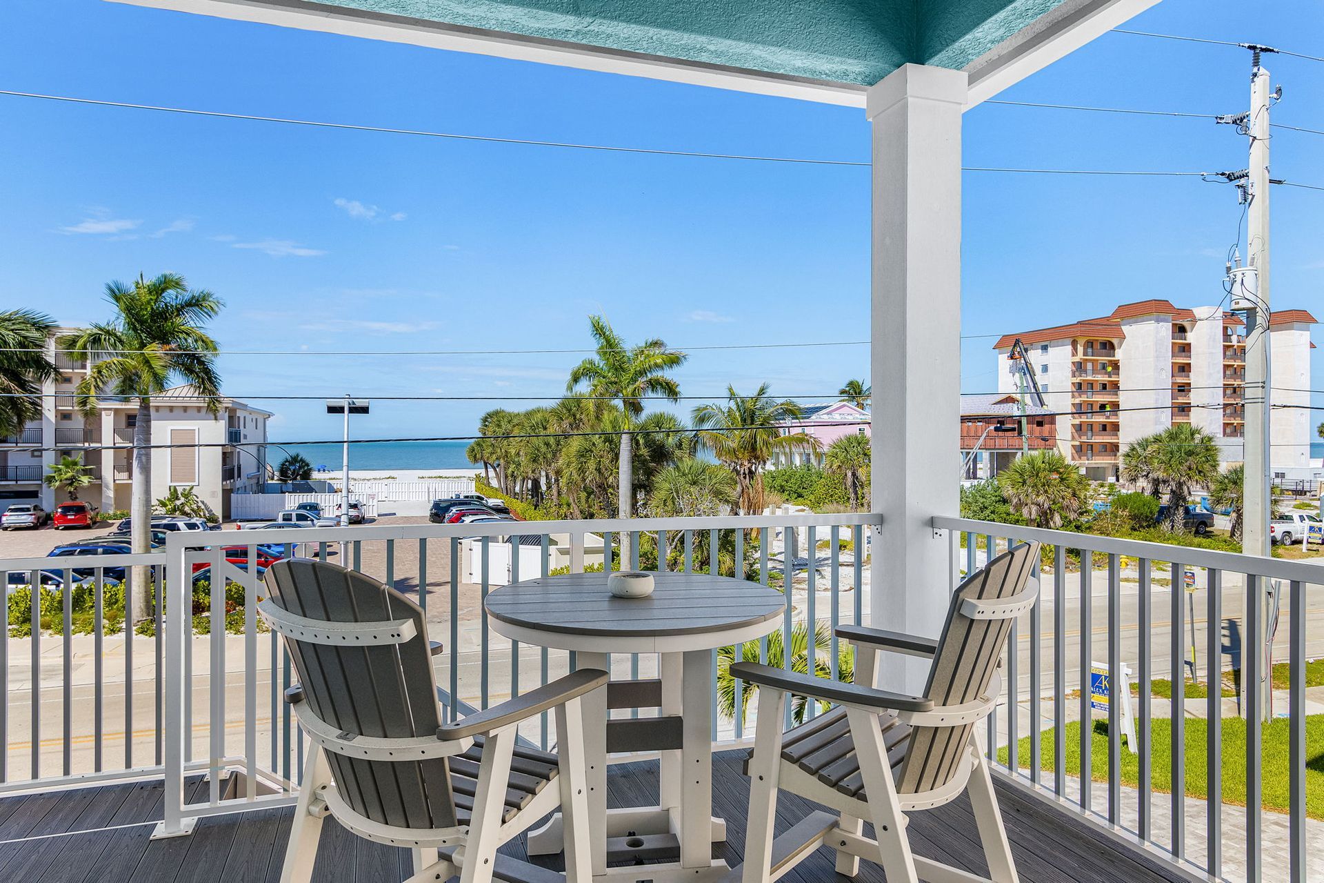 Balcony with white chairs and table overlooking a beach and ocean under a blue sky