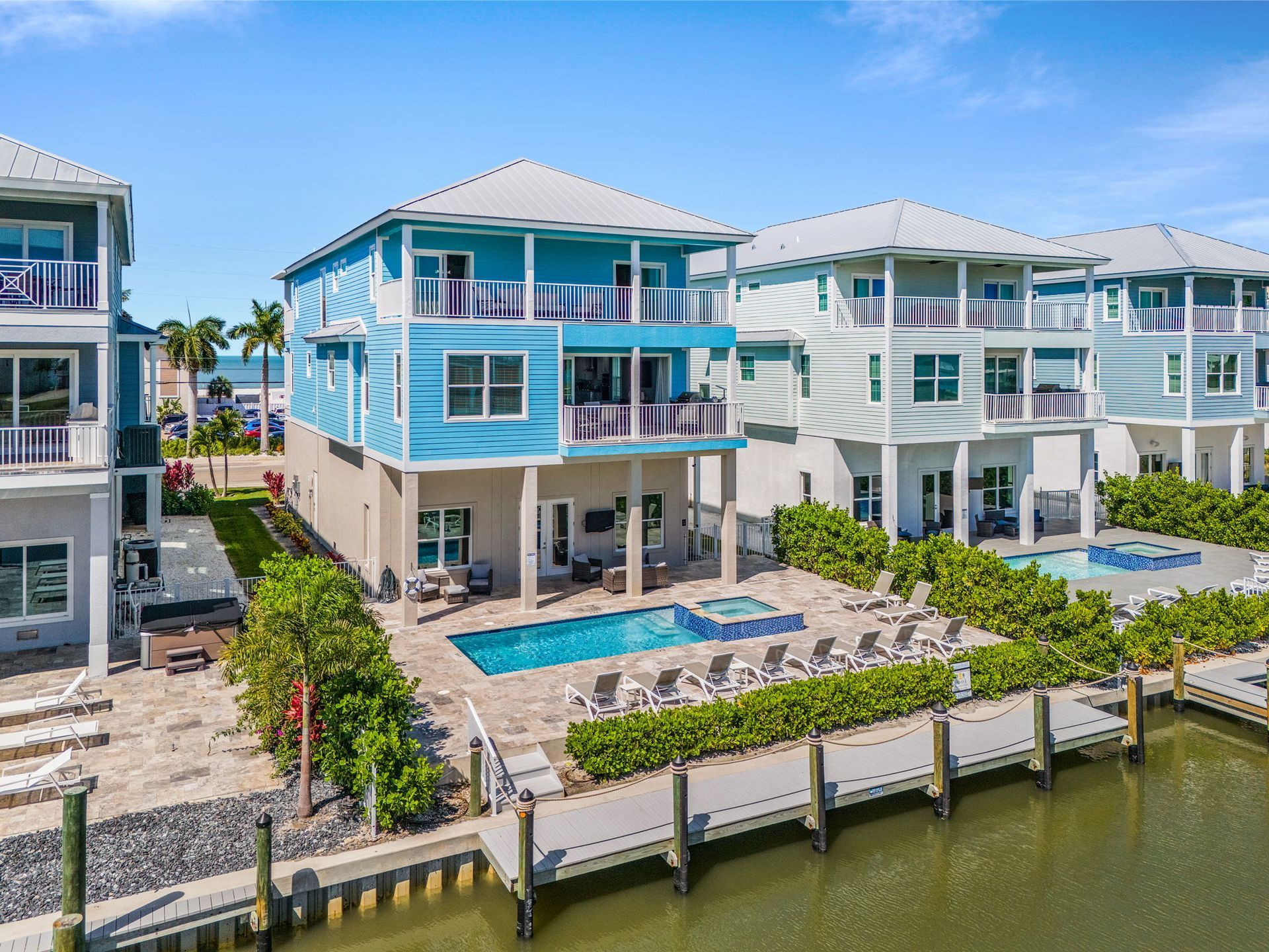 Waterfront blue and white beachfront homes with docks, pools, and balconies under a clear sky