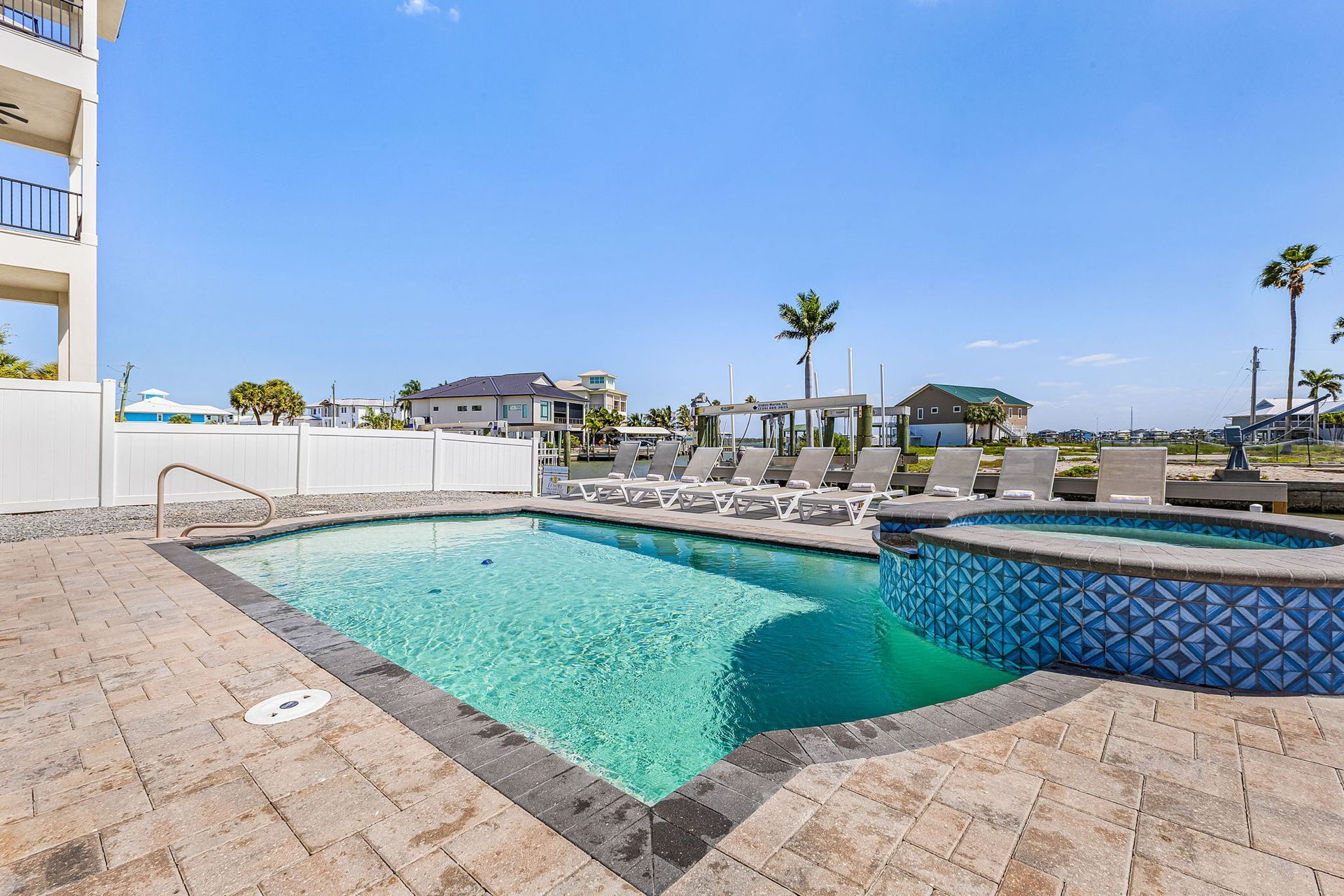Outdoor swimming pool with turquoise water and blue tile, beside a sun deck and lounge chairs under a clear sky
