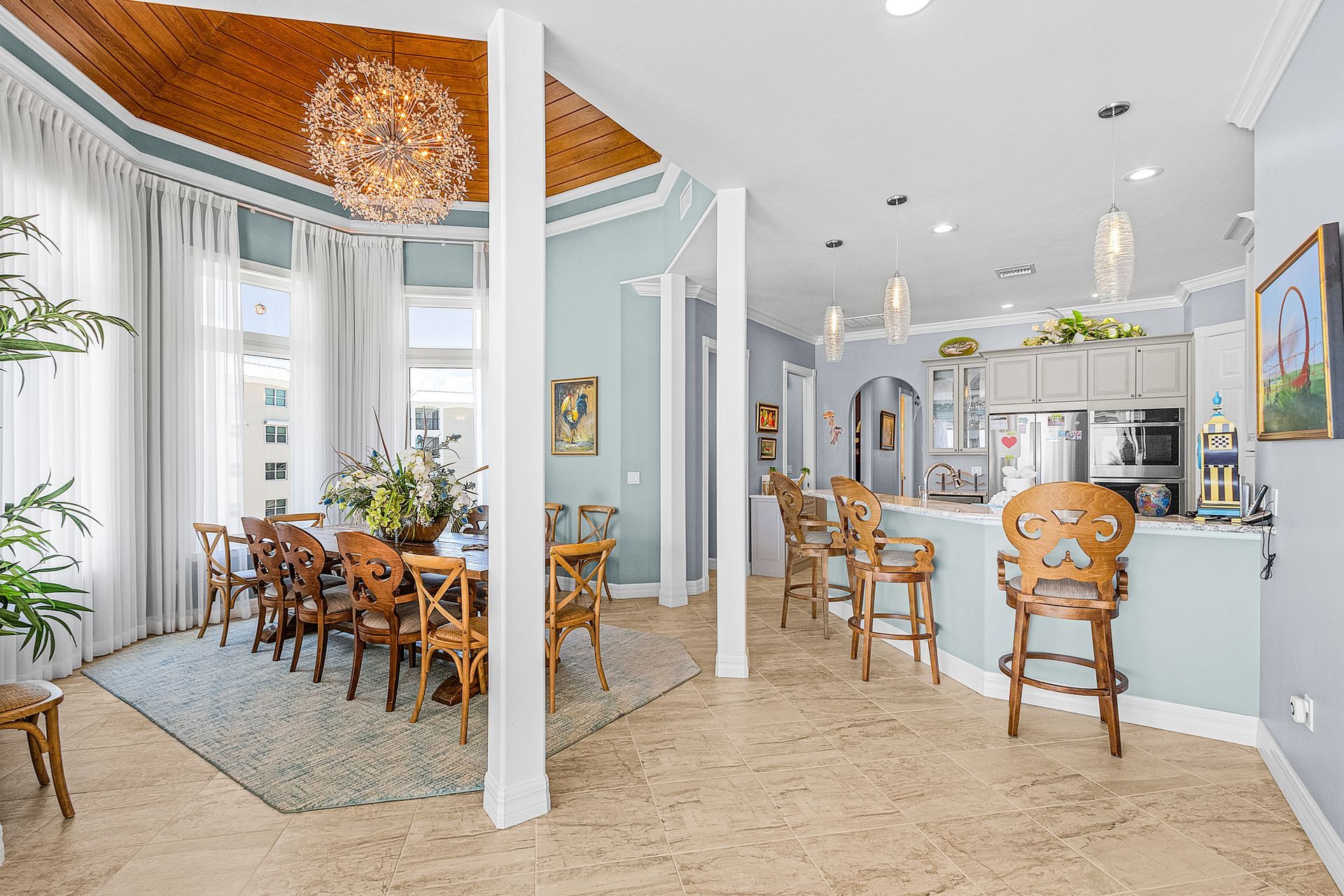 Bright, elegant dining room with ornate wooden chairs, pale blue walls, tall windows, and marble floors