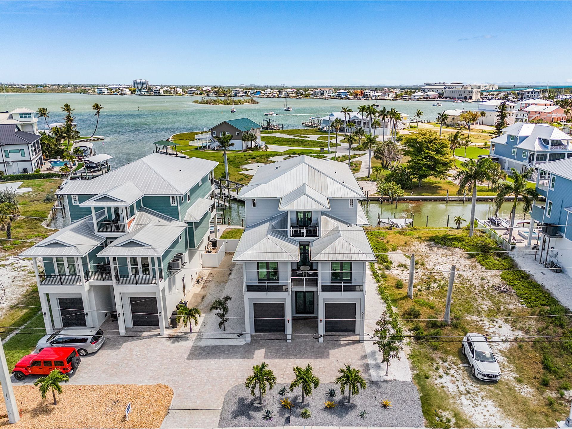 Aerial view of modern waterfront houses with docks, palm trees, and a canal under clear skies