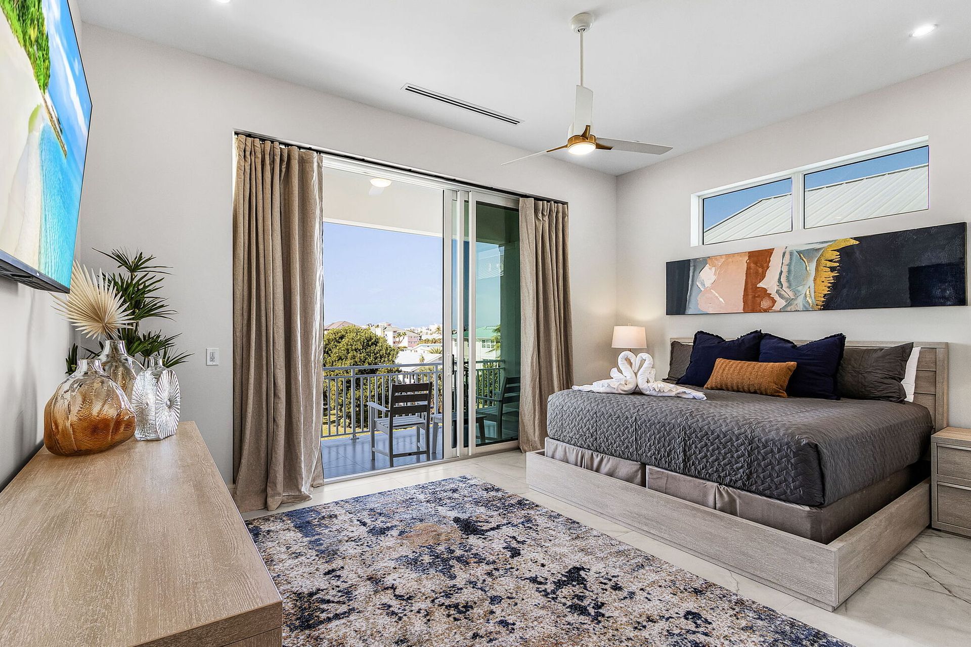 Bright modern bedroom with gray bed, patterned rug, and sliding doors to a balcony view.