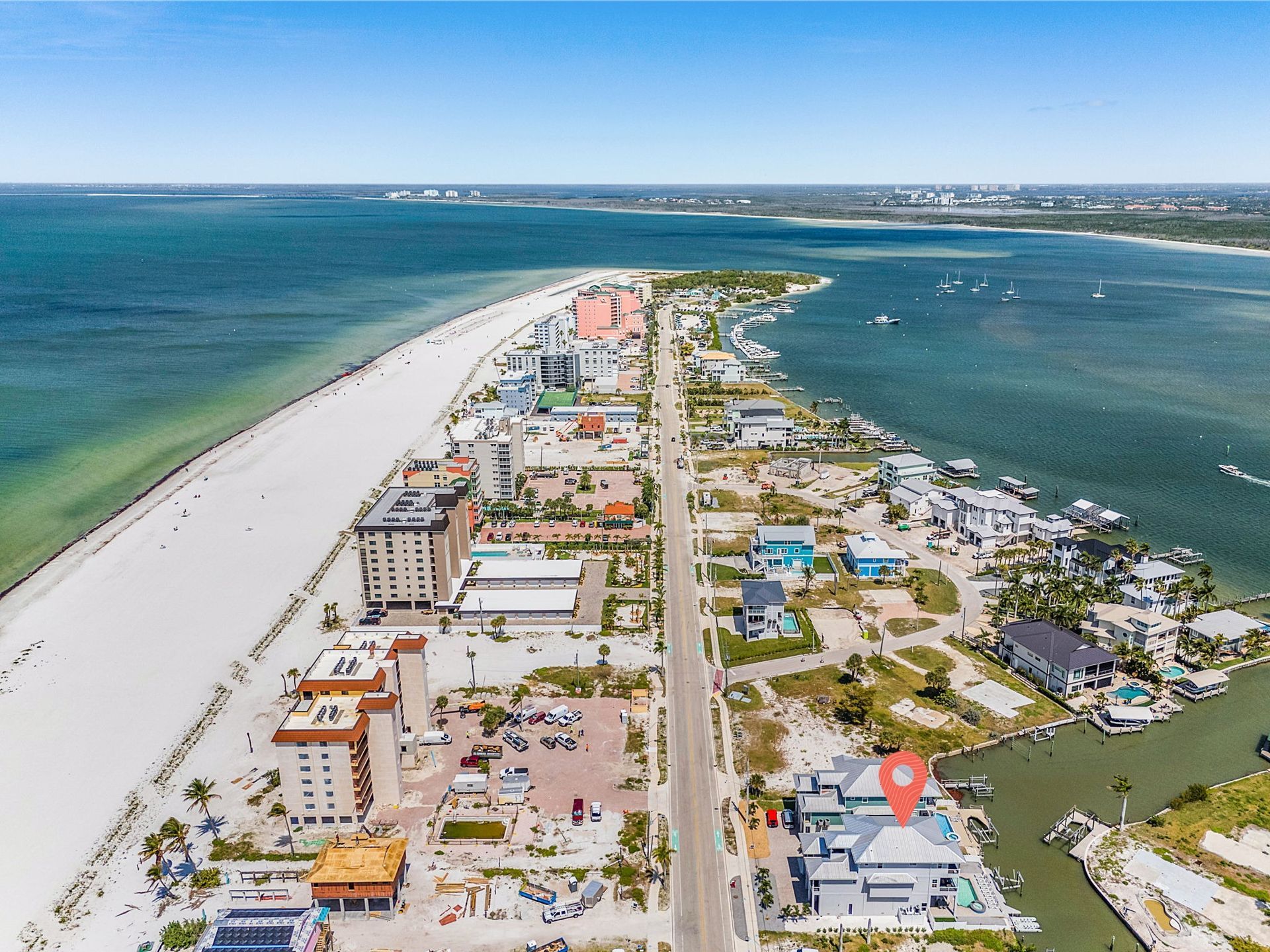 Aerial view of a narrow coastal town between blue ocean waters and a long white sand beach.