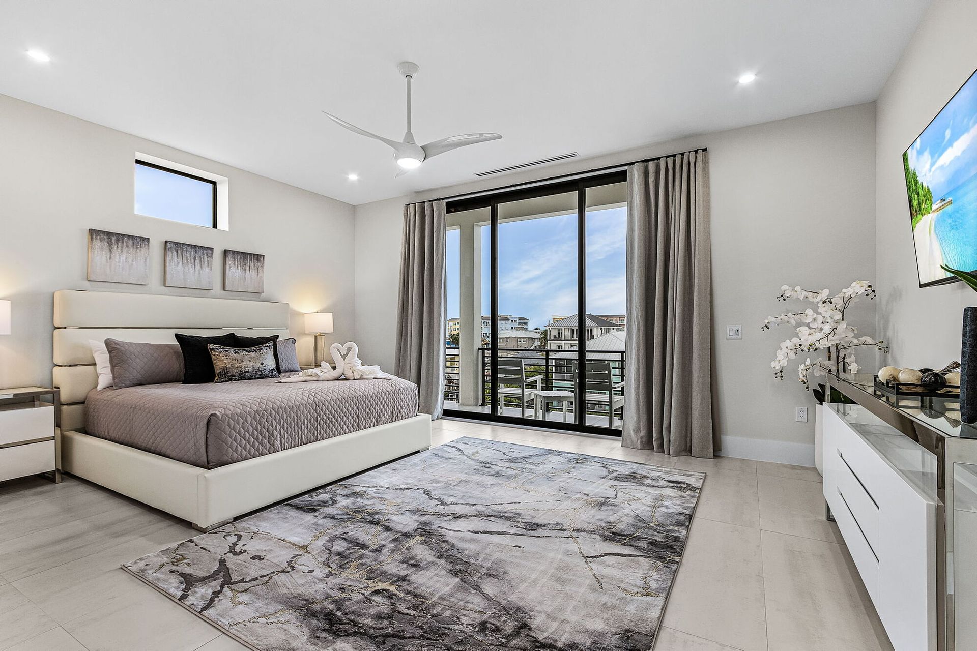 Bright modern bedroom with a large bed, gray rug, sliding doors, and a balcony view.