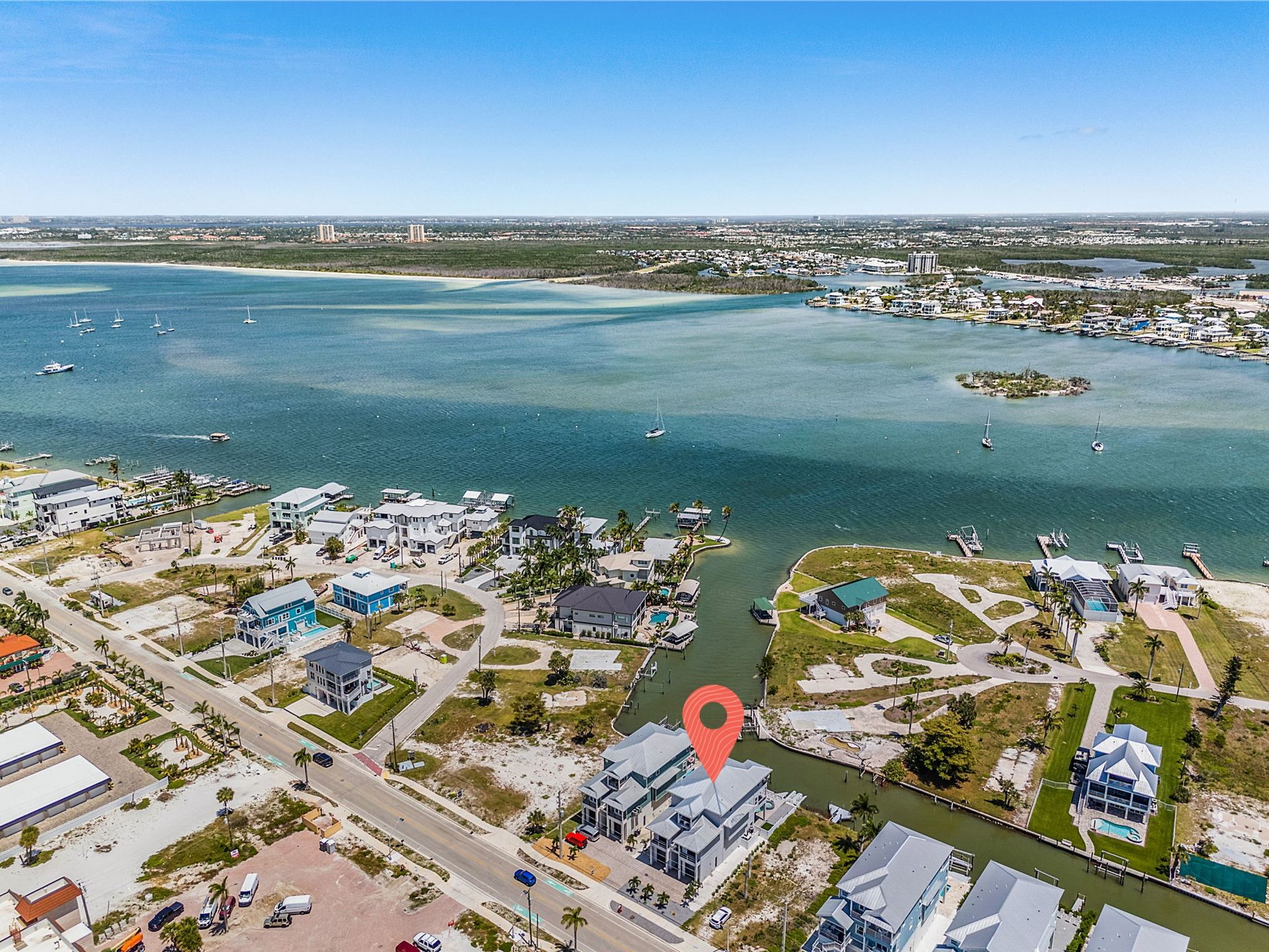 Aerial view of a coastal neighborhood with blue water, boats, docks, and a red location pin on a waterfront building