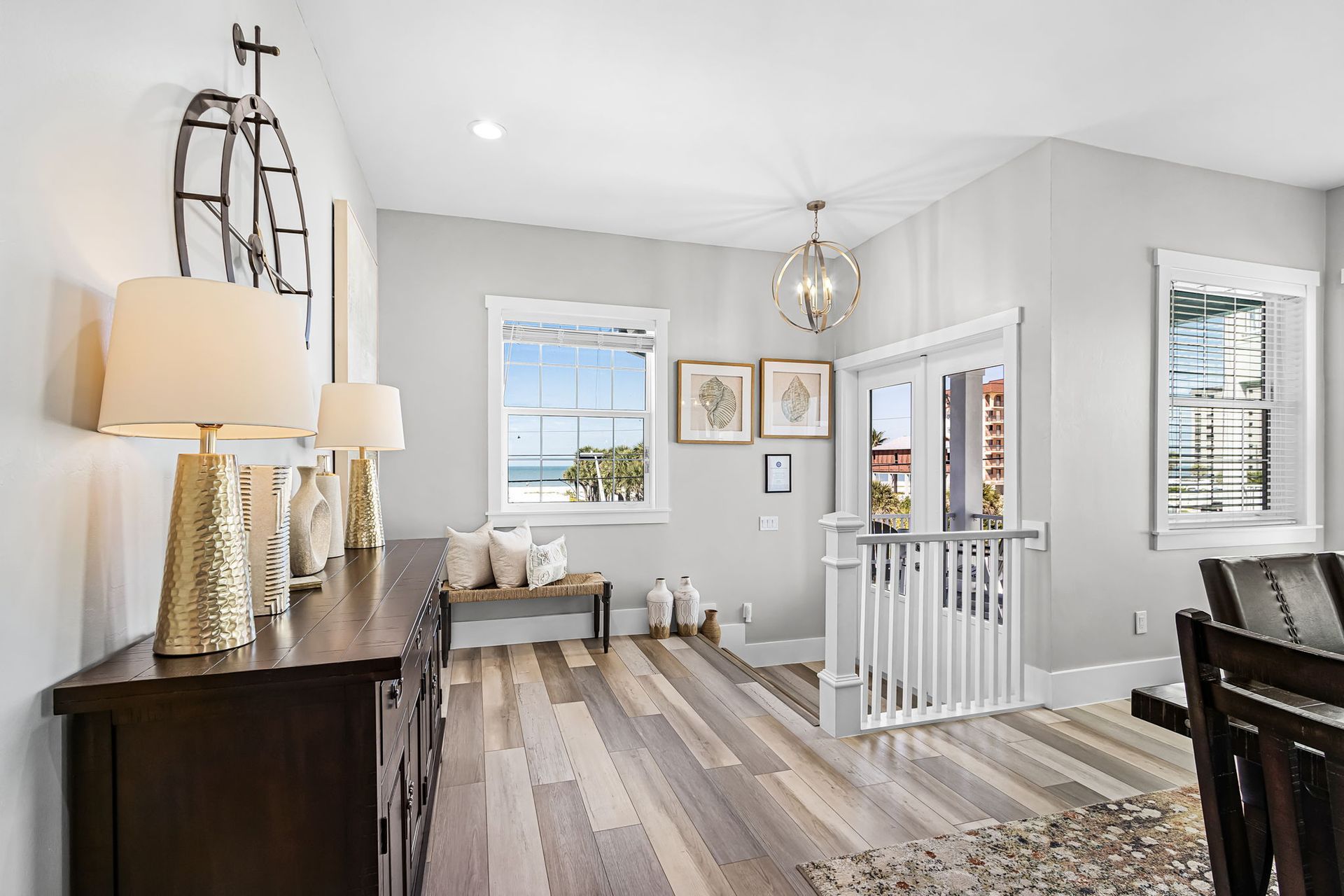 Bright entryway with gray walls, wood floors, console table, lamps, bench, and staircase railing