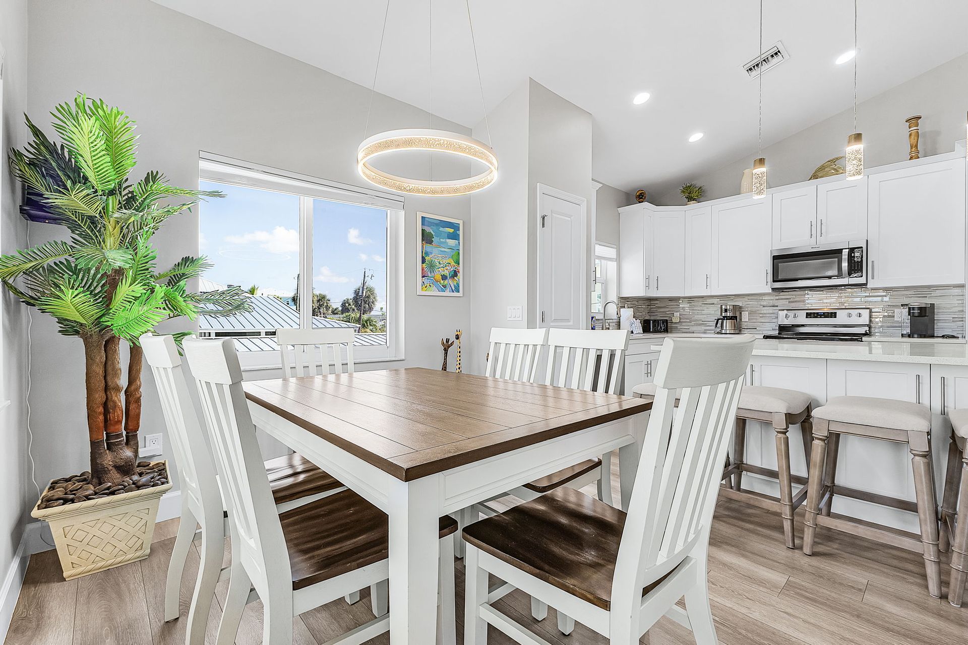 Bright modern dining and kitchen area with white chairs, wood table, and large windows