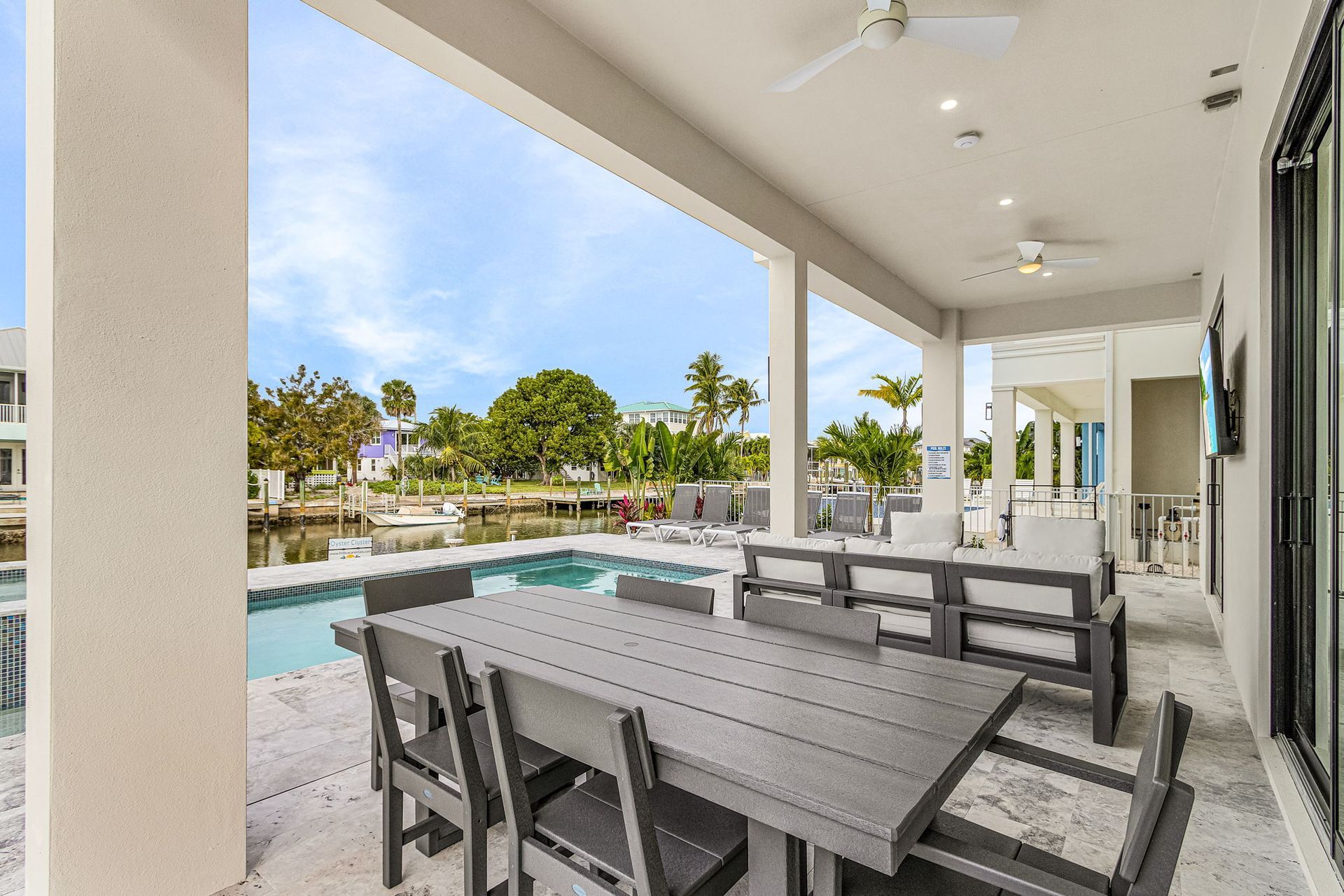 Covered patio with dining table, seating, and pool view on a sunny day.