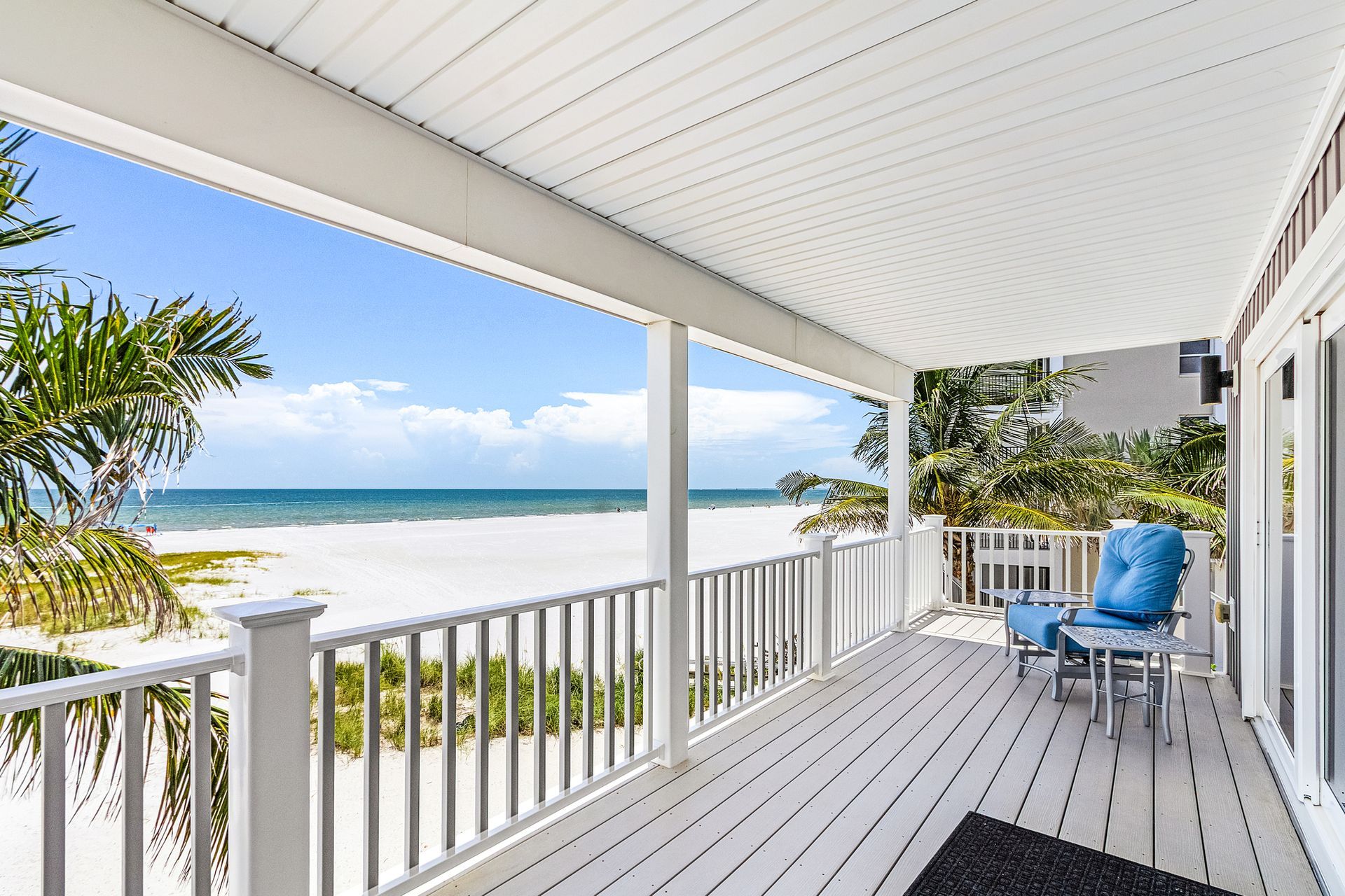 Covered seaside porch with white railing, blue chairs, and ocean view