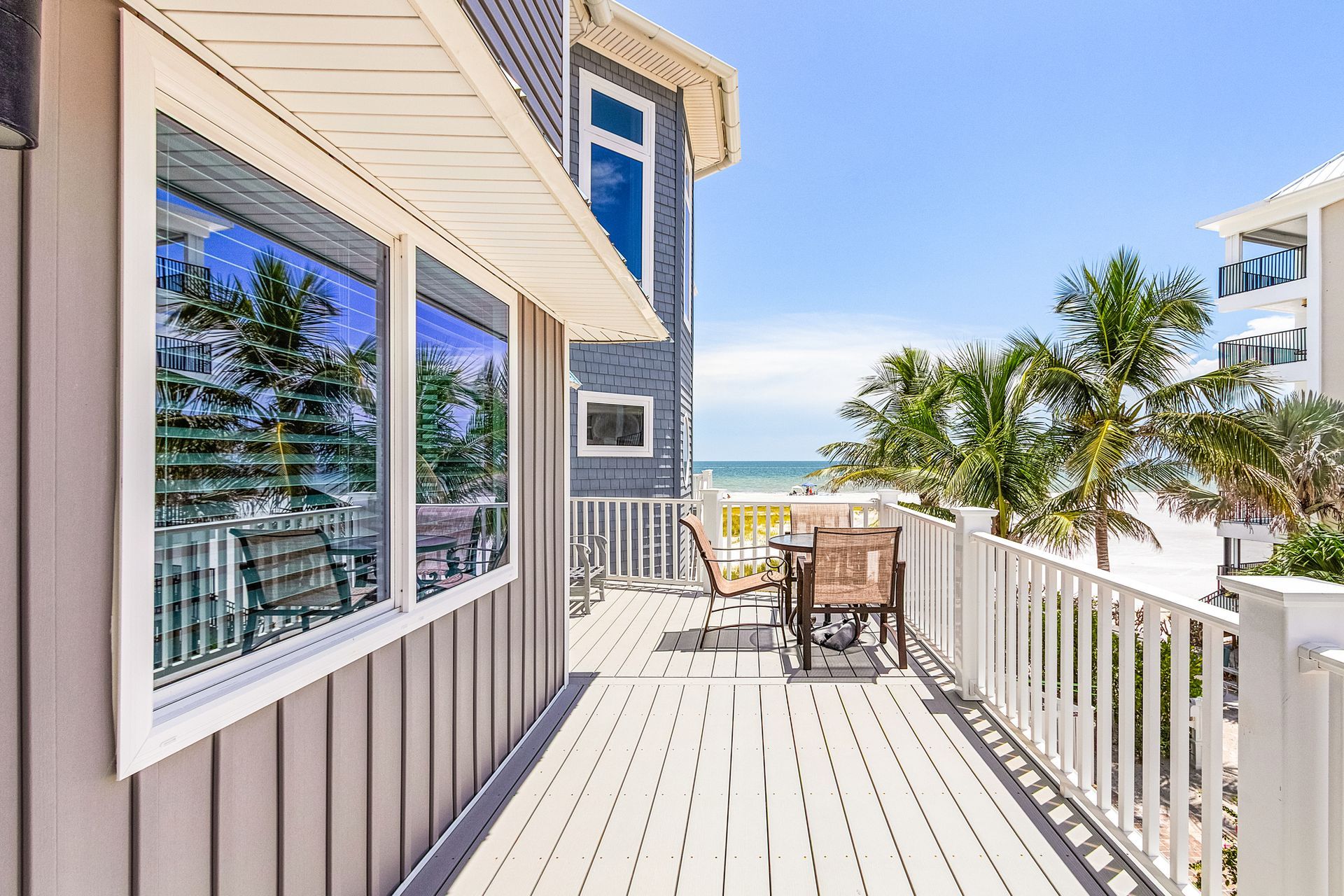 Bright coastal deck with white railing, patio table, and ocean view beside a house