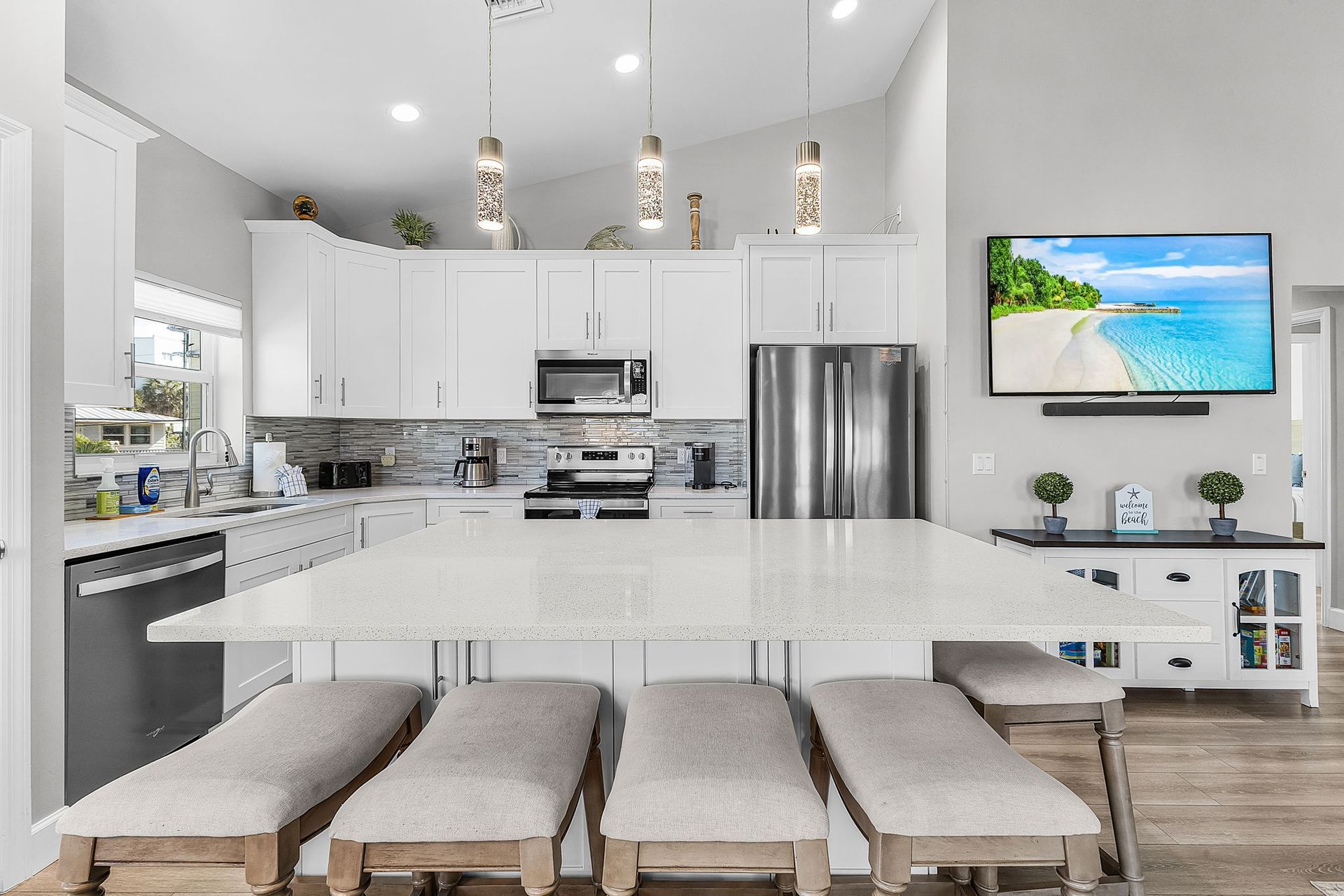 Bright modern kitchen with white cabinets, large island, bar stools, and a wall-mounted TV