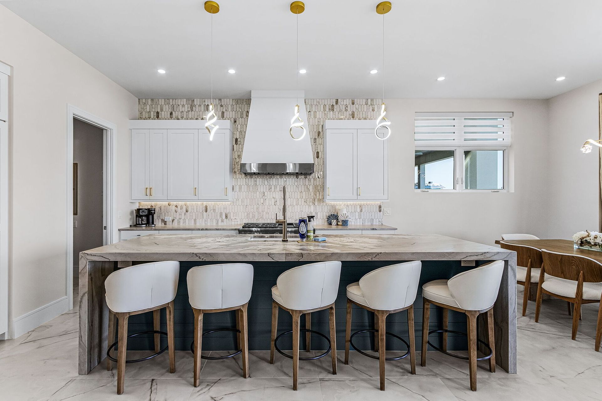 Bright white kitchen with marble island, five stools, pendant lights, and open dining area