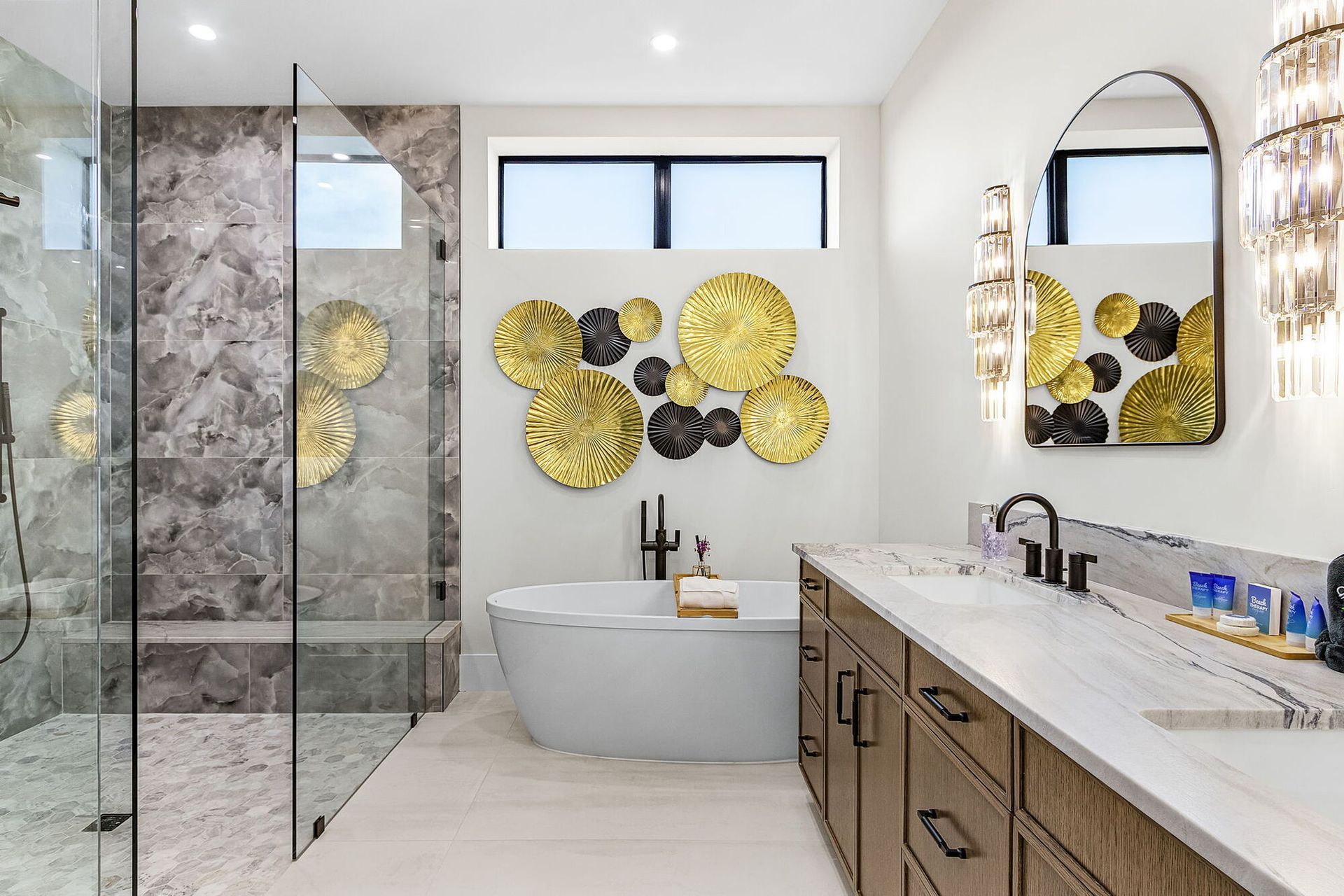 Modern bathroom with glass shower, freestanding tub, double vanity, and gold wall decor