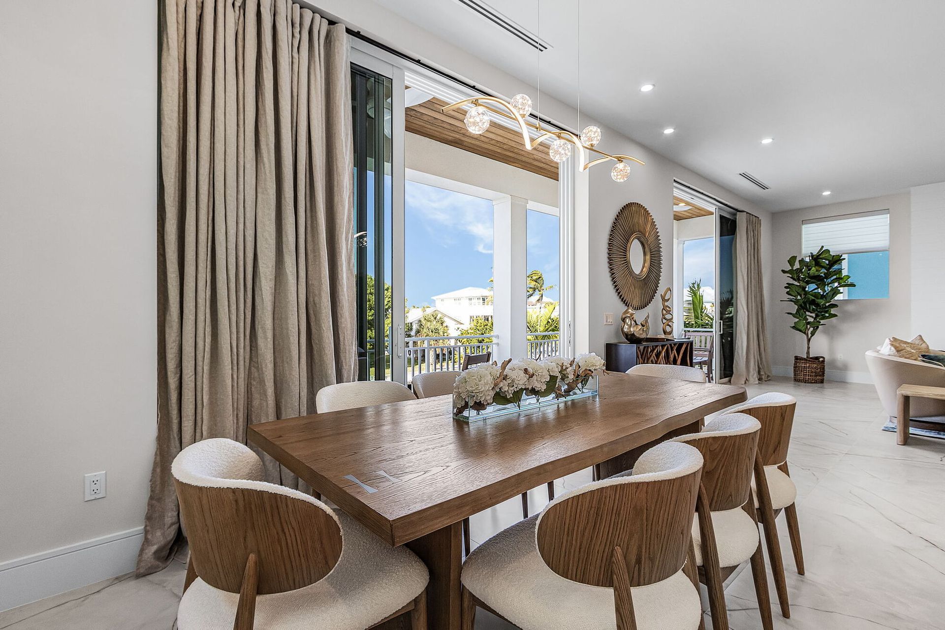 Bright dining room with a wooden table, woven chairs, large windows, and neutral decor
