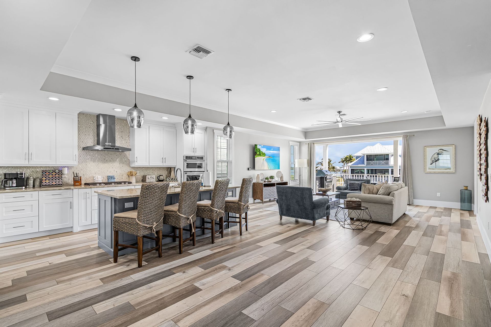 Open-plan kitchen and living room with white cabinets, gray wood floors, island seating, and sectional sofa.