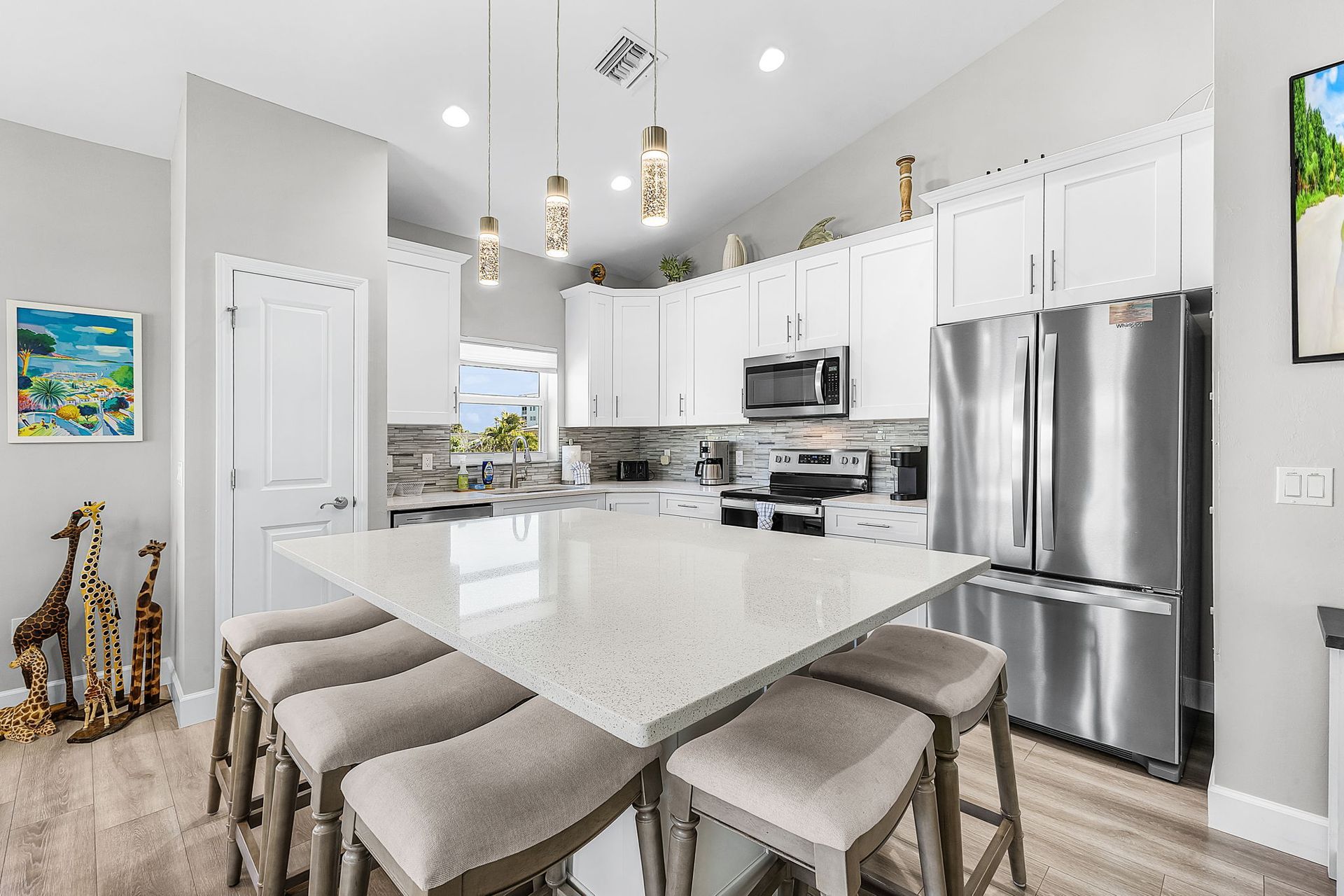 Bright modern kitchen with white cabinets, stainless steel appliances, and a marble island with bar stools