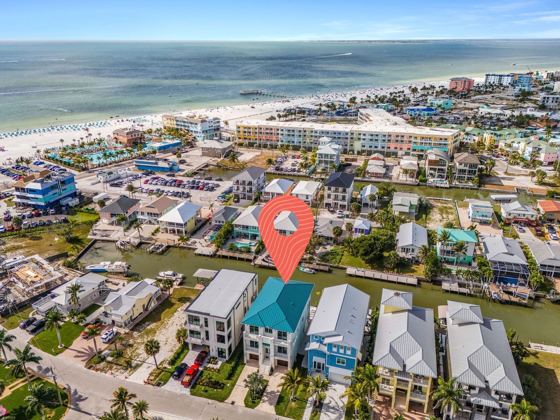 Aerial view of a beachfront neighborhood with a red location pin over blue-roofed houses by the shore.