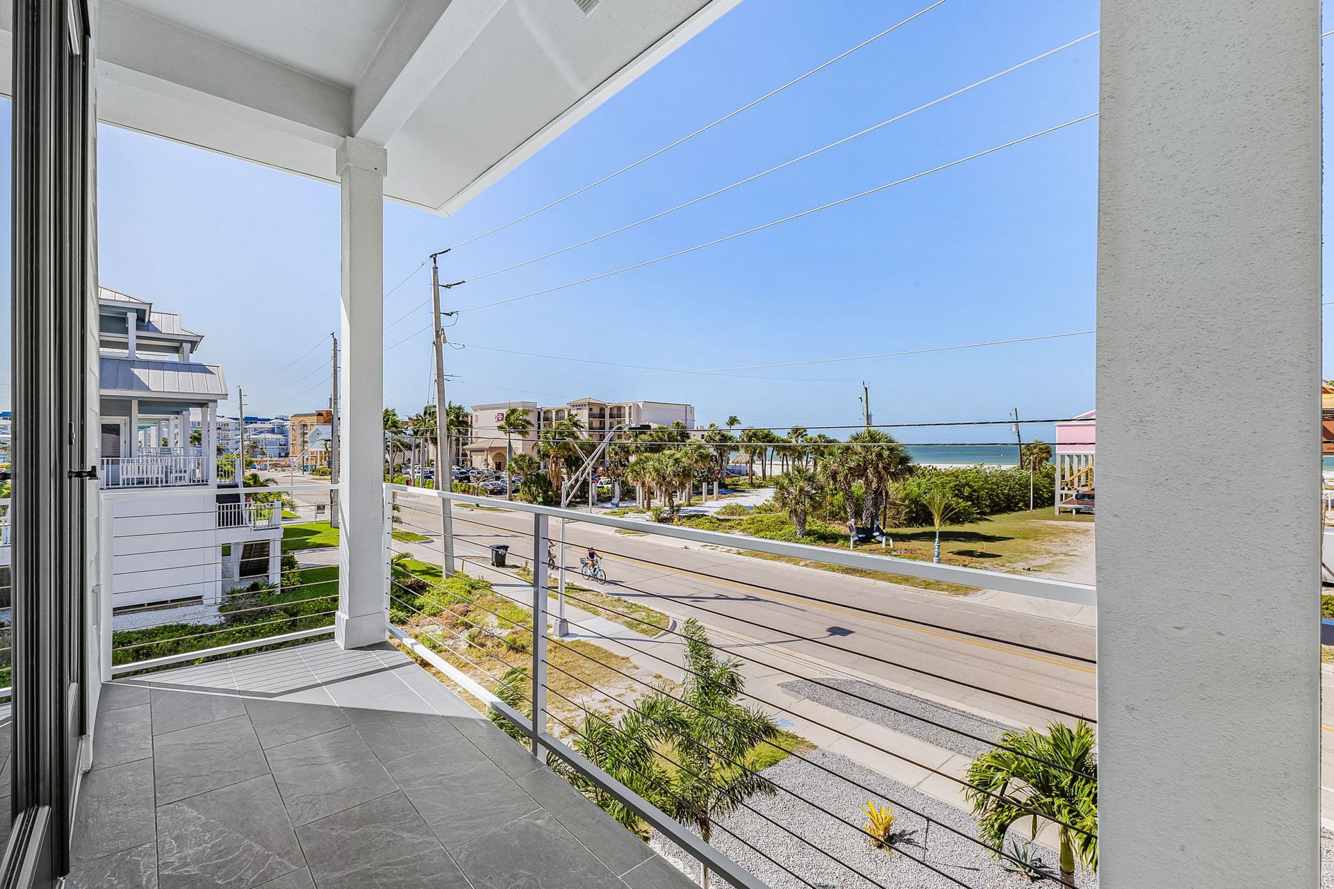 Balcony view of a coastal road, palm trees, and ocean under a bright sky