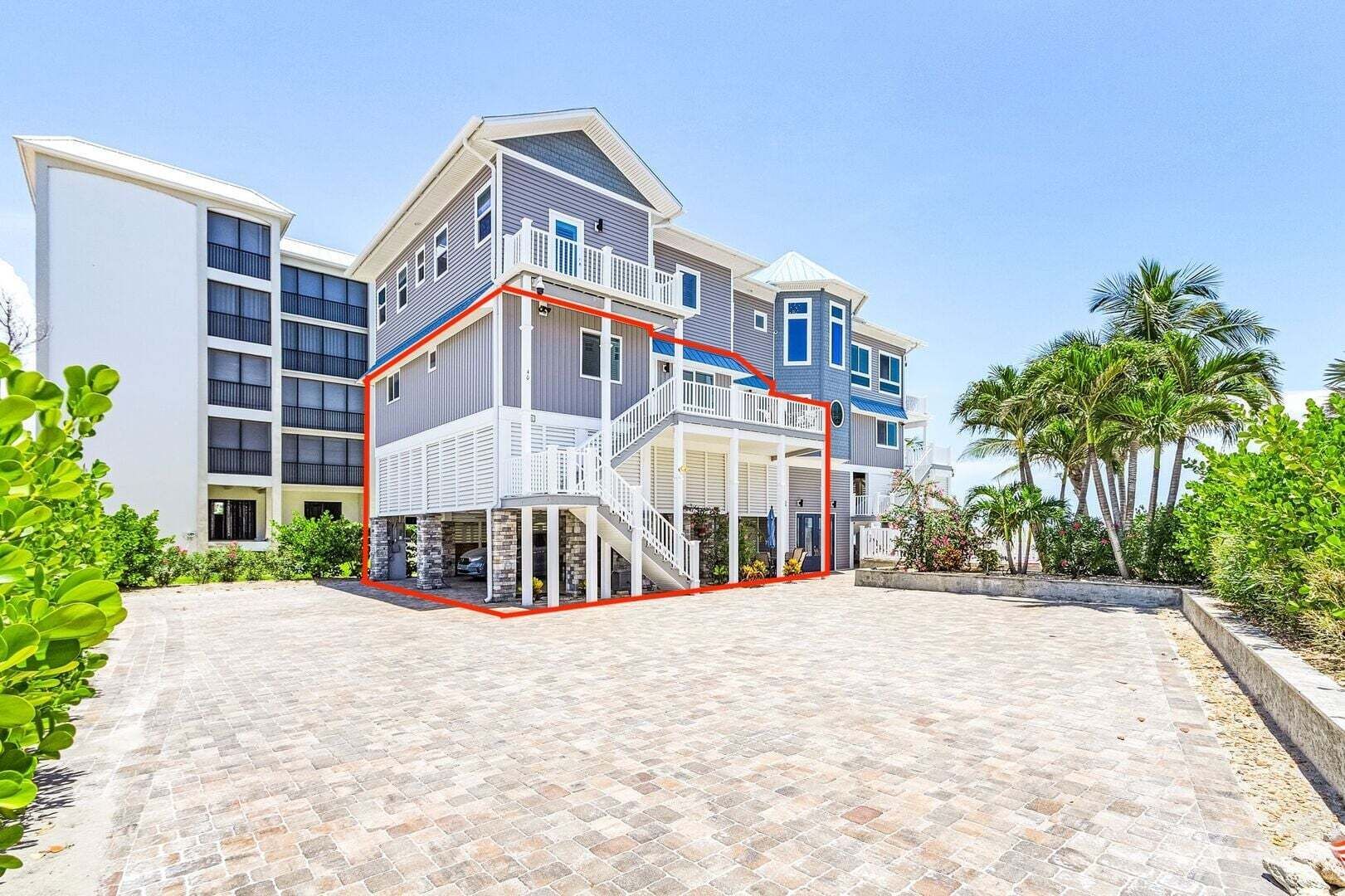 Modern beachfront house with white and blue exterior, red trim, and sandy driveway