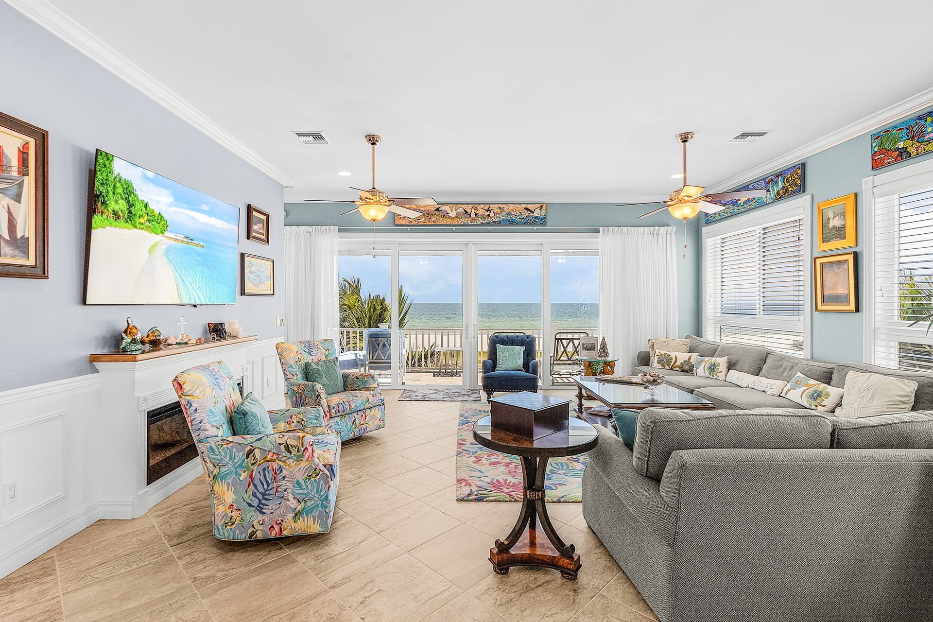 Bright coastal living room with floral chairs, gray sofa, ocean view, and colorful wall art