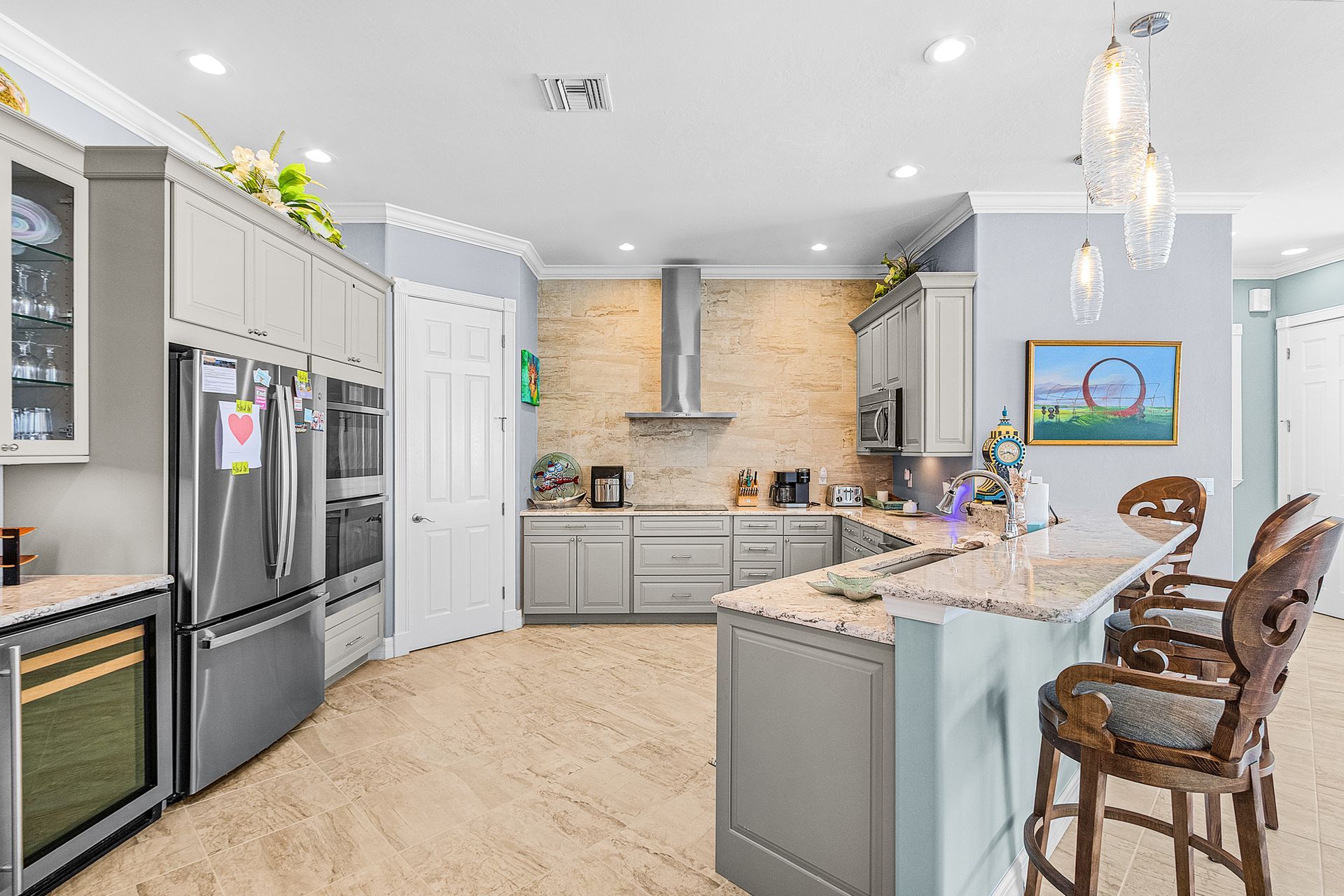 Modern gray kitchen with stainless appliances, island seating, white cabinets, and bright pendant lights