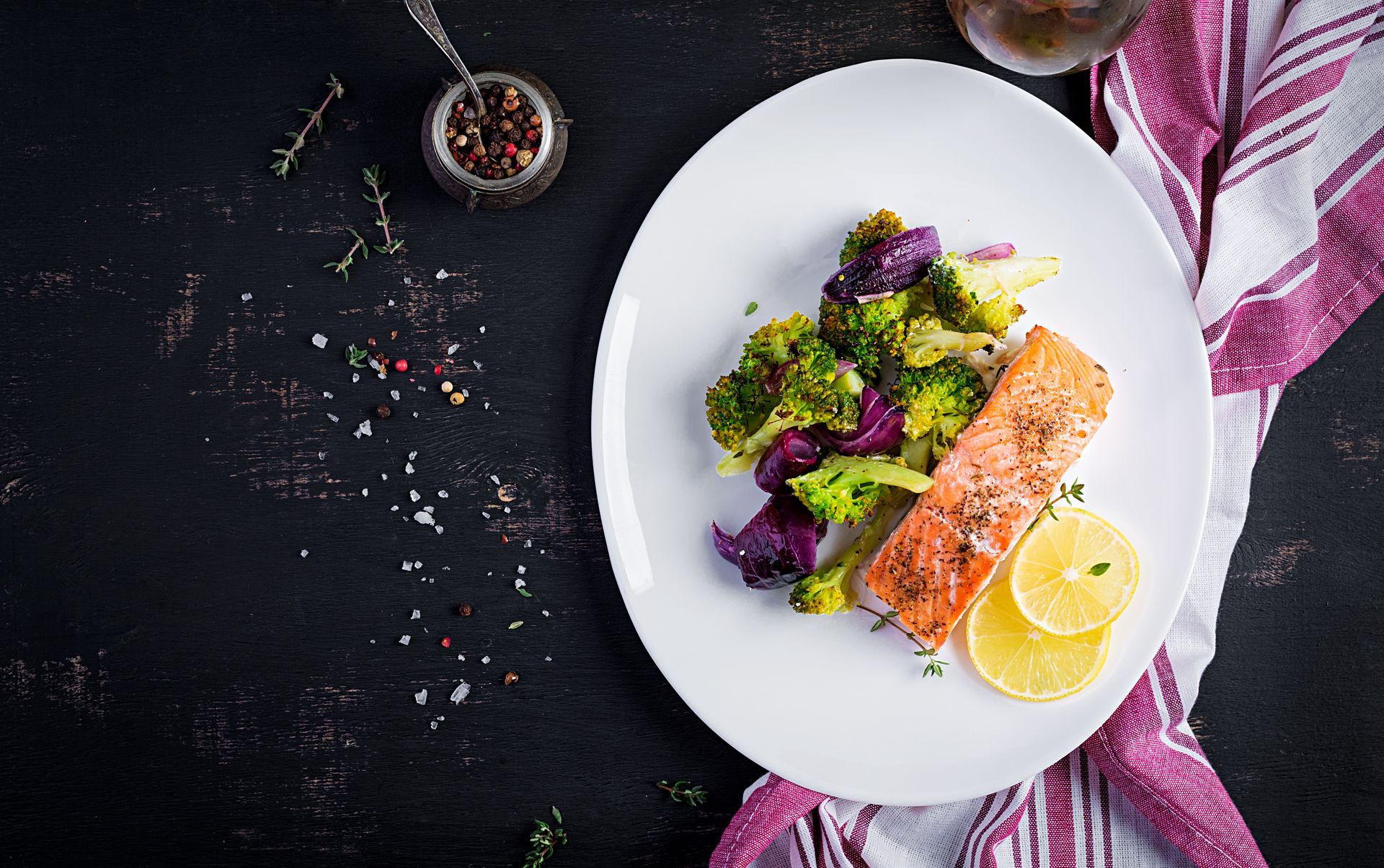 Salmon fillet with roasted broccoli and lemon slices on a white plate.