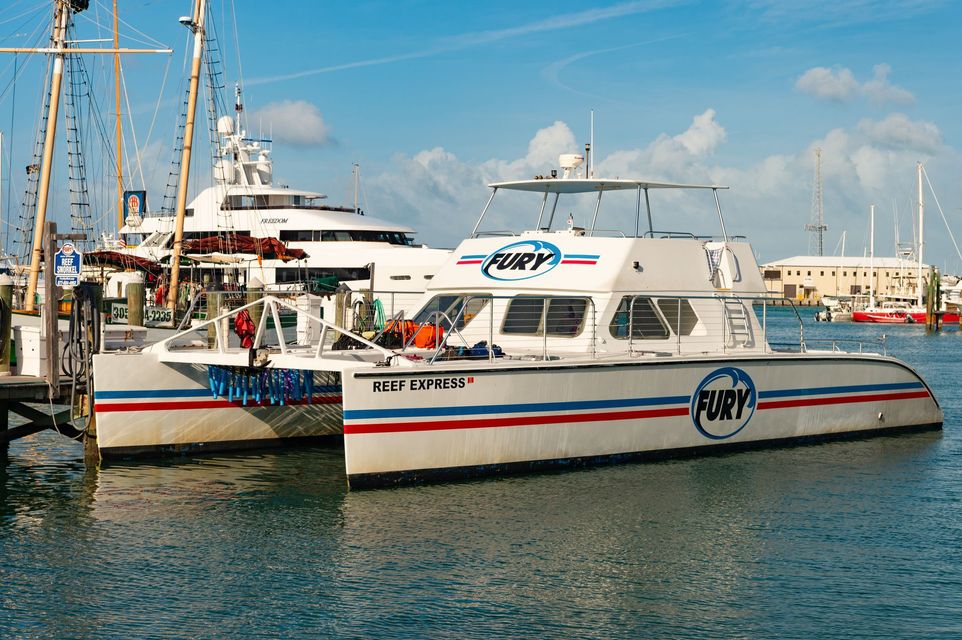 Catamaran boat "Fury" docked in marina, blue water, white hull with red/blue stripes.