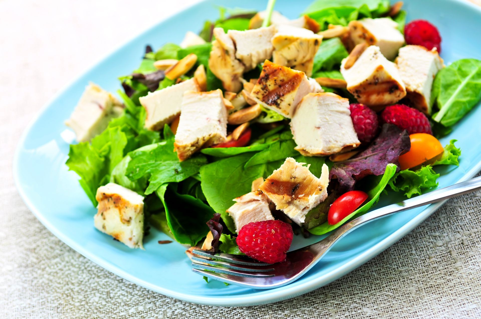 Chicken salad with raspberries, tomatoes, and almond slices on a blue plate.