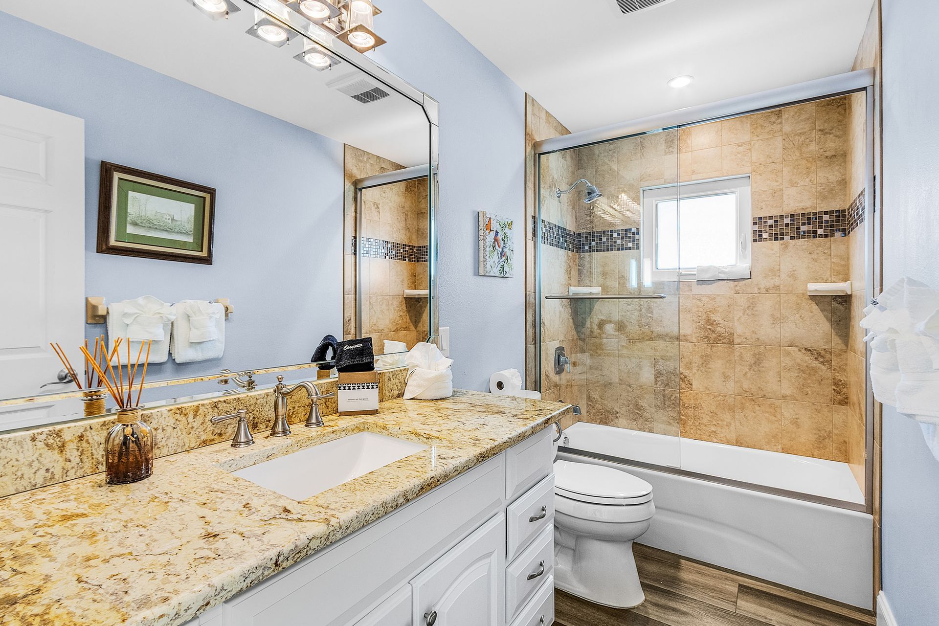 Bright bathroom with granite vanity, large mirror, beige tile shower, and white toilet.