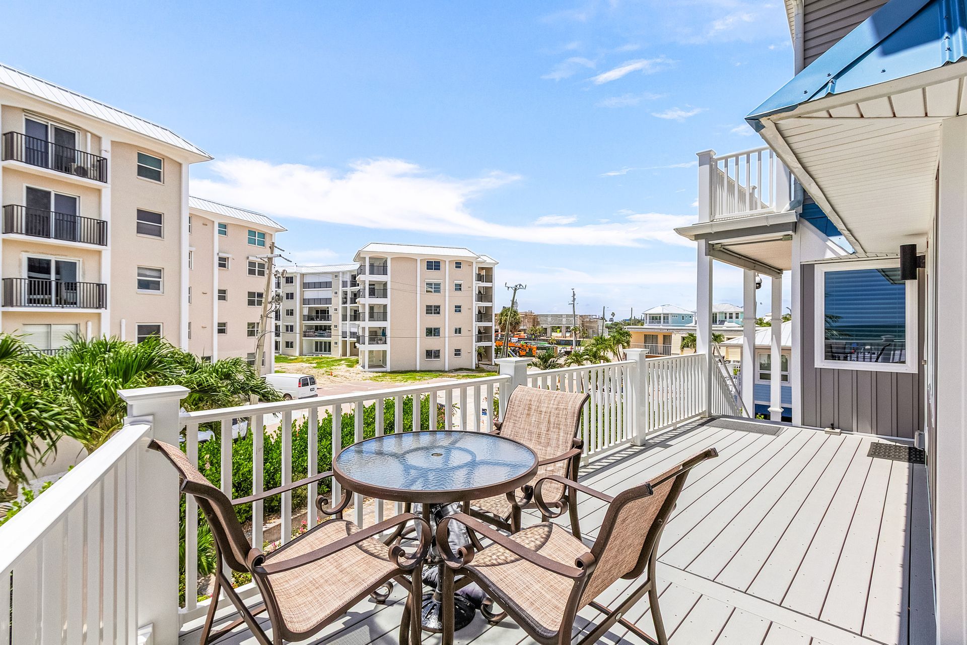 Balcony with glass table and chairs overlooking resort-style apartment buildings under a bright blue sky