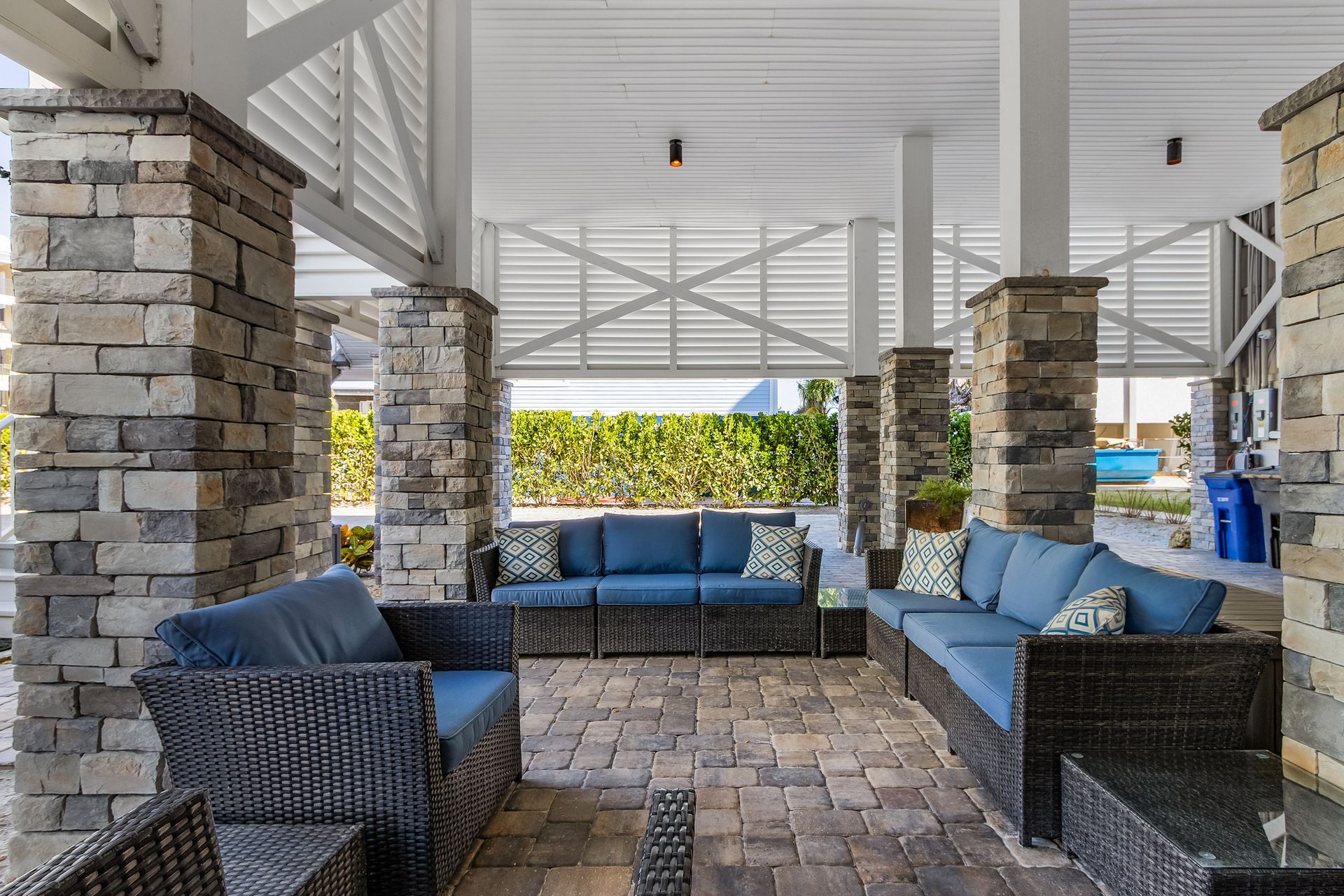 Covered outdoor patio with wicker sofas, blue cushions, stone columns, and a white roof