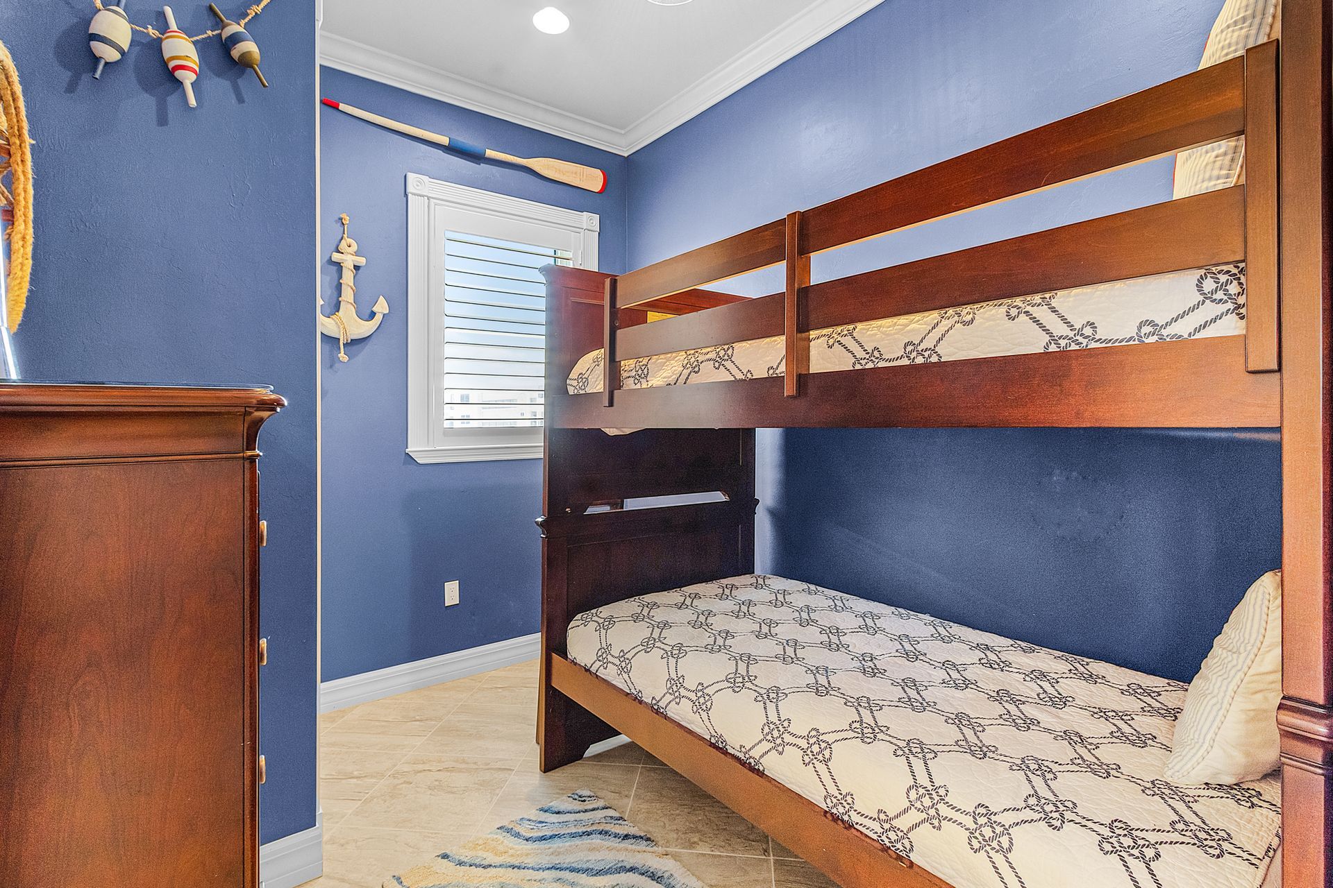 Blue children's bedroom with wooden bunk bed, white window blinds, and dresser