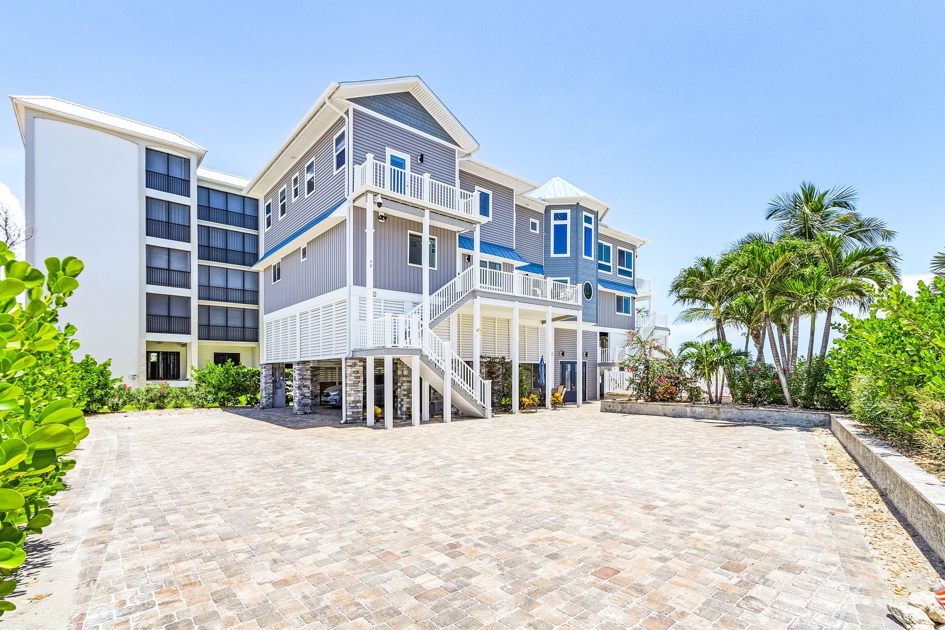 Modern beach house with white stilts and balconies on a sandy lot under a clear blue sky