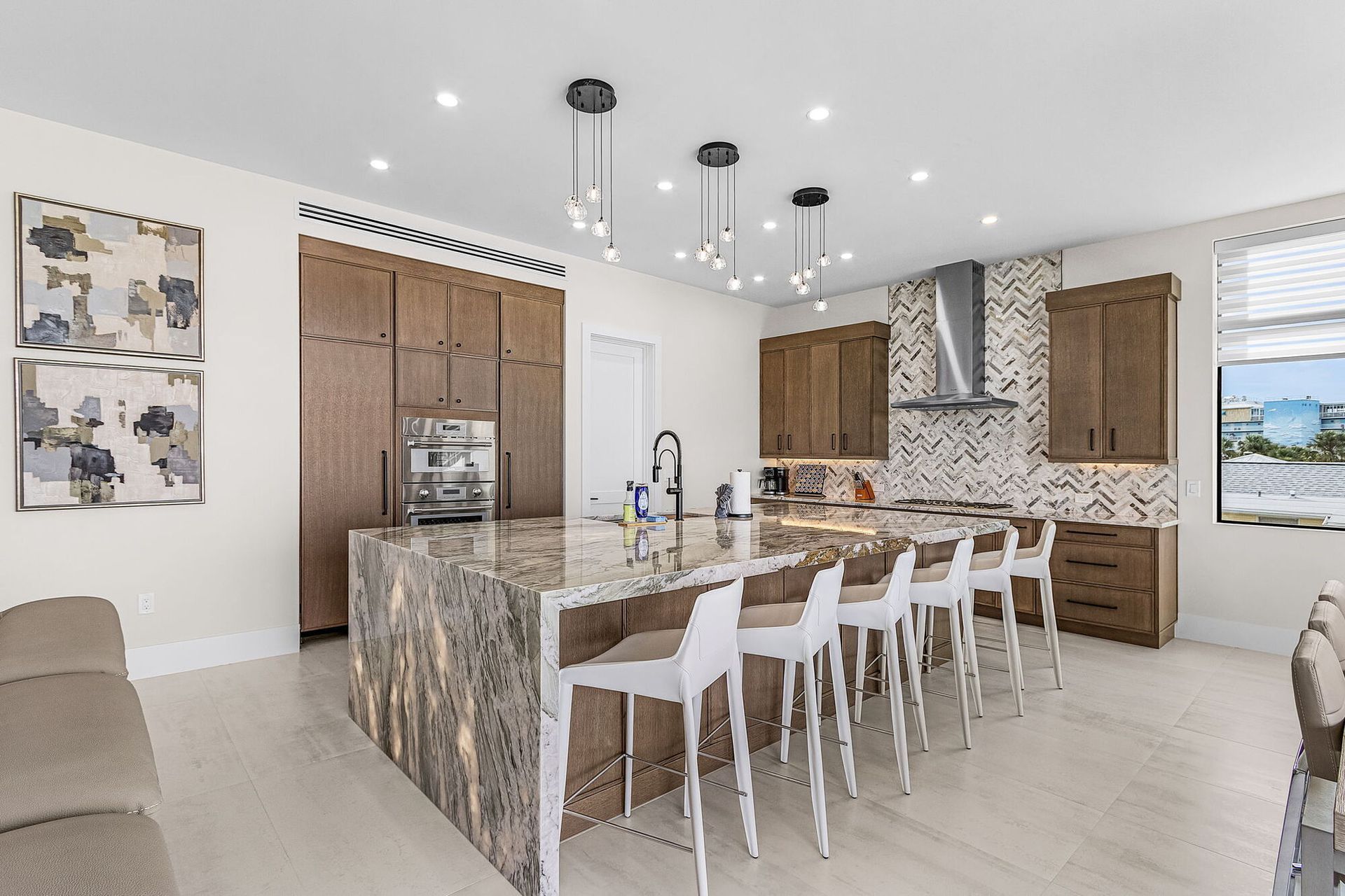 Modern kitchen with marble island, white bar stools, wood cabinets, and pendant lights
