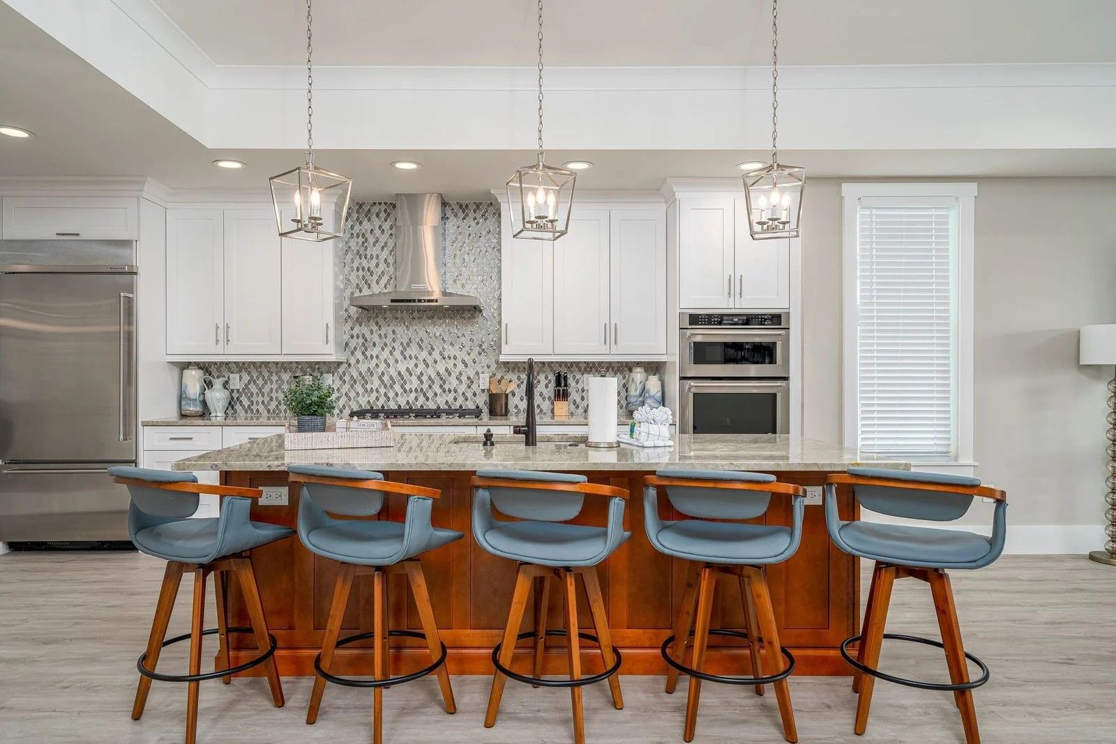 Bright modern kitchen with a large island, blue stools, white cabinets, and pendant lights