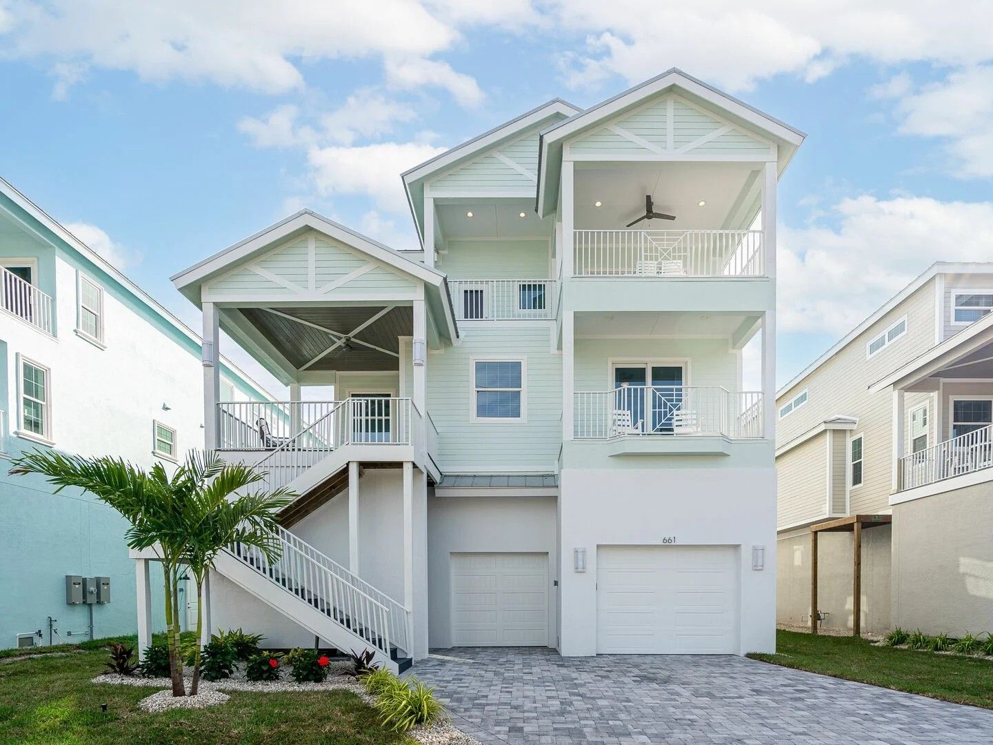 Two-story white beach house with balconies, stairs, and garage under a blue sky.