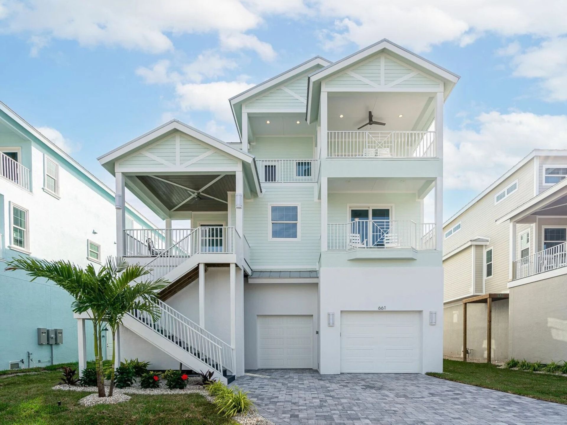 Pastel beach house with stilted balconies, stairs, and garage under a blue sky